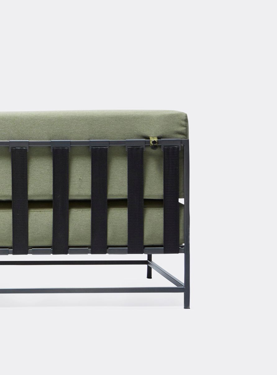 a steel framed sofa with black metal finish and green cushions and supporting belts on a white background .