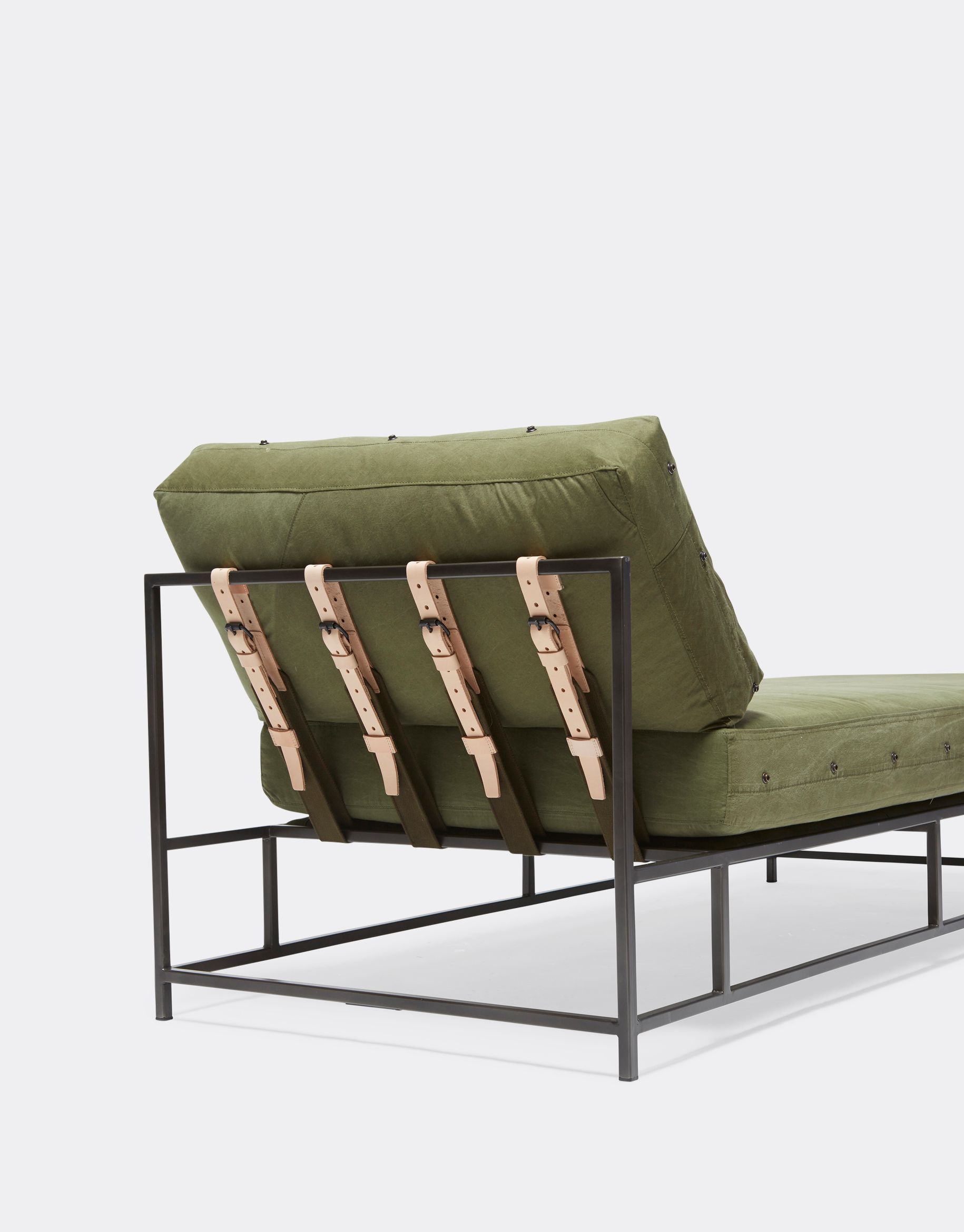 a green chaise with a metal frame and leather straps on a white background .
