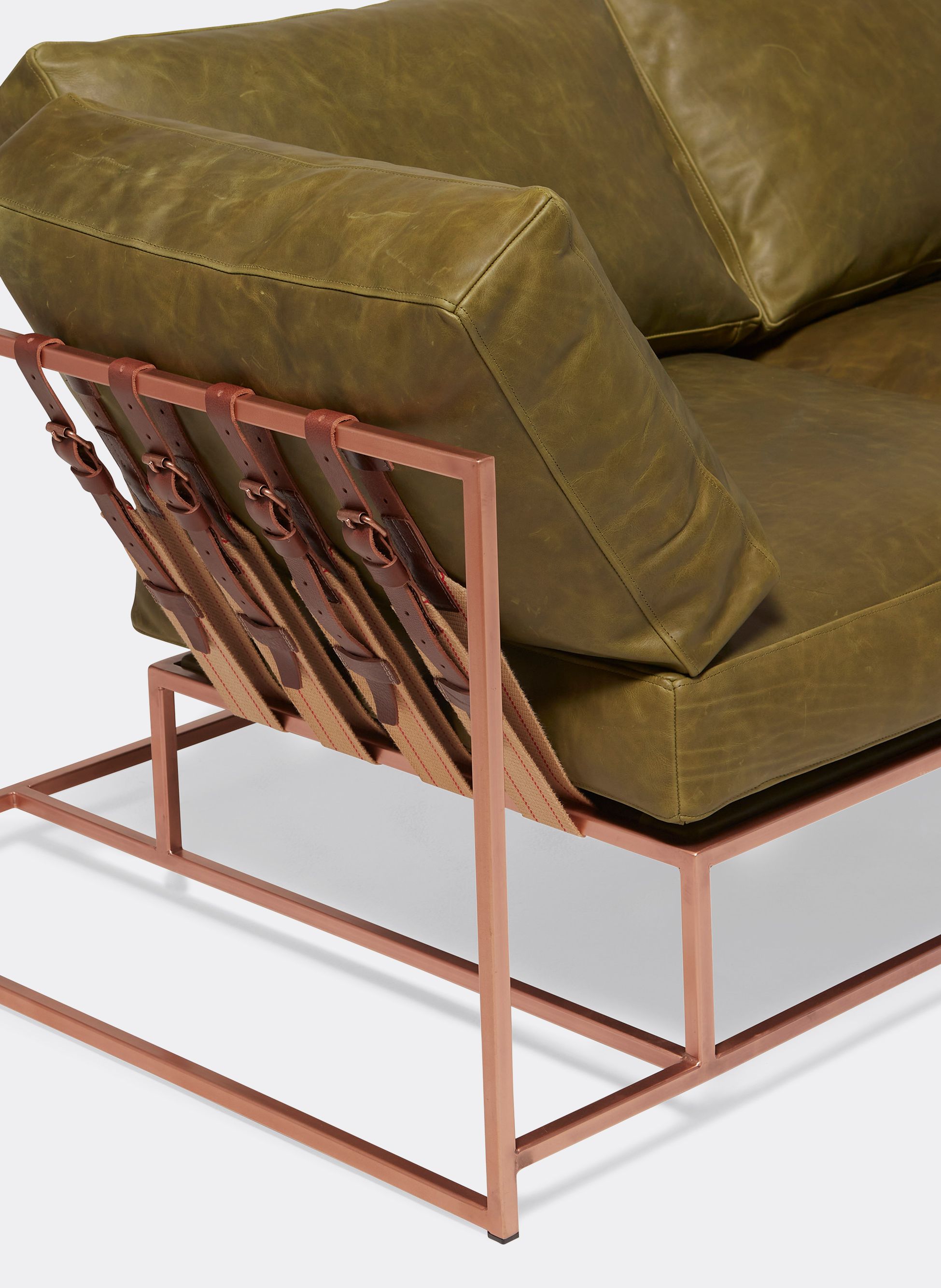 a green leather couch with a copper finished steel frame with supporting belts shown on a white background .