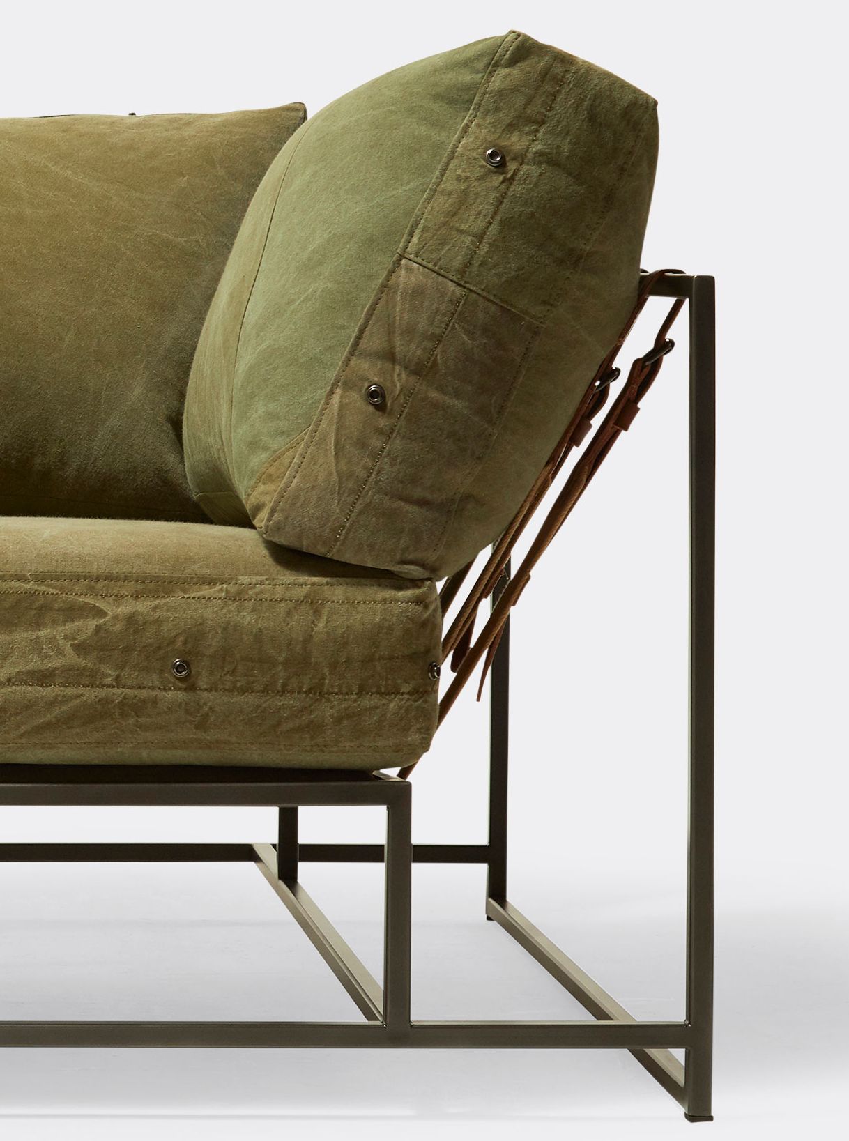 a green canvas upholstered sofa on a black steel frame with supporting belts shown on a white background .