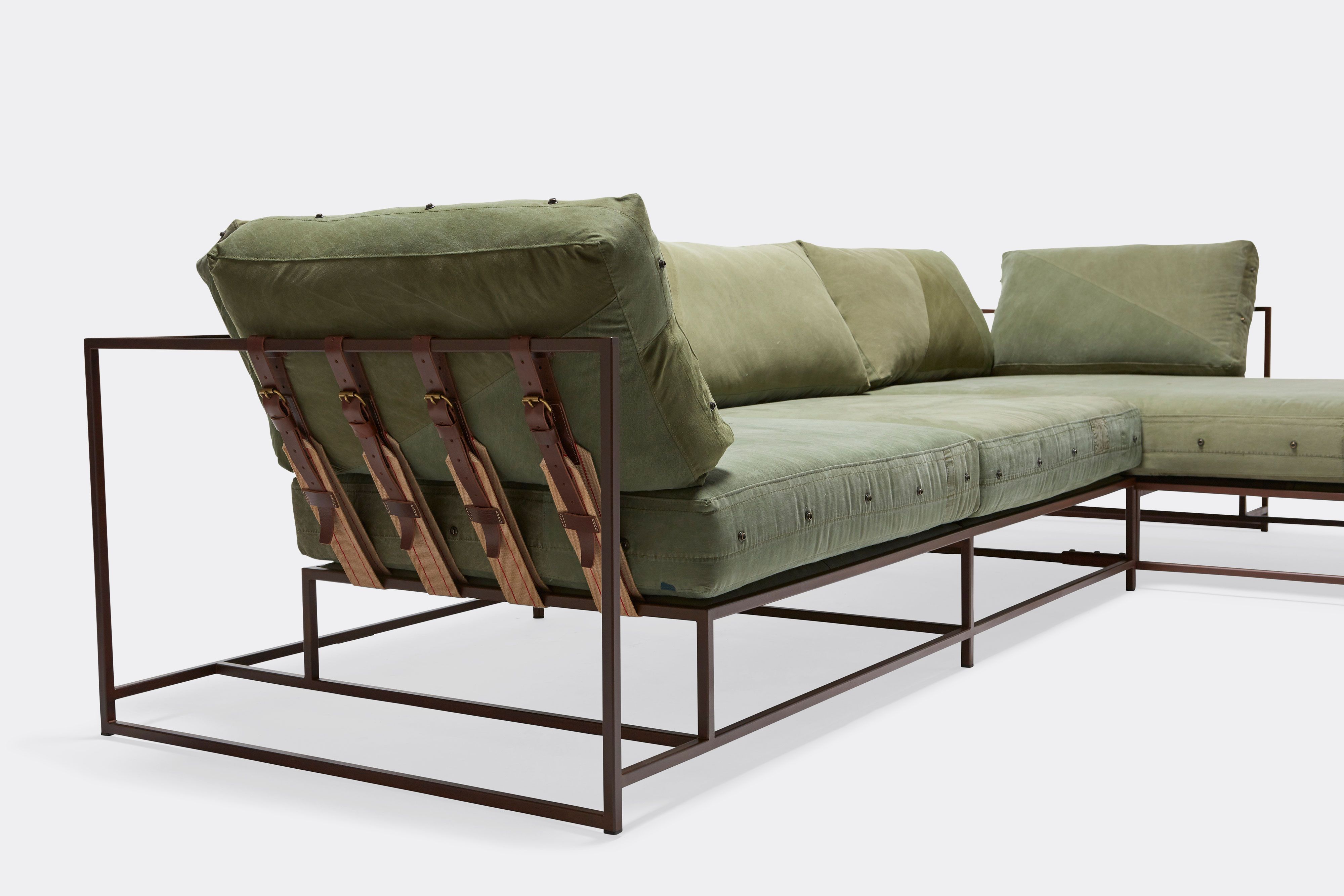a green sectional sofa with a brown steel frame and leather and webbing supporting belts on a white background .