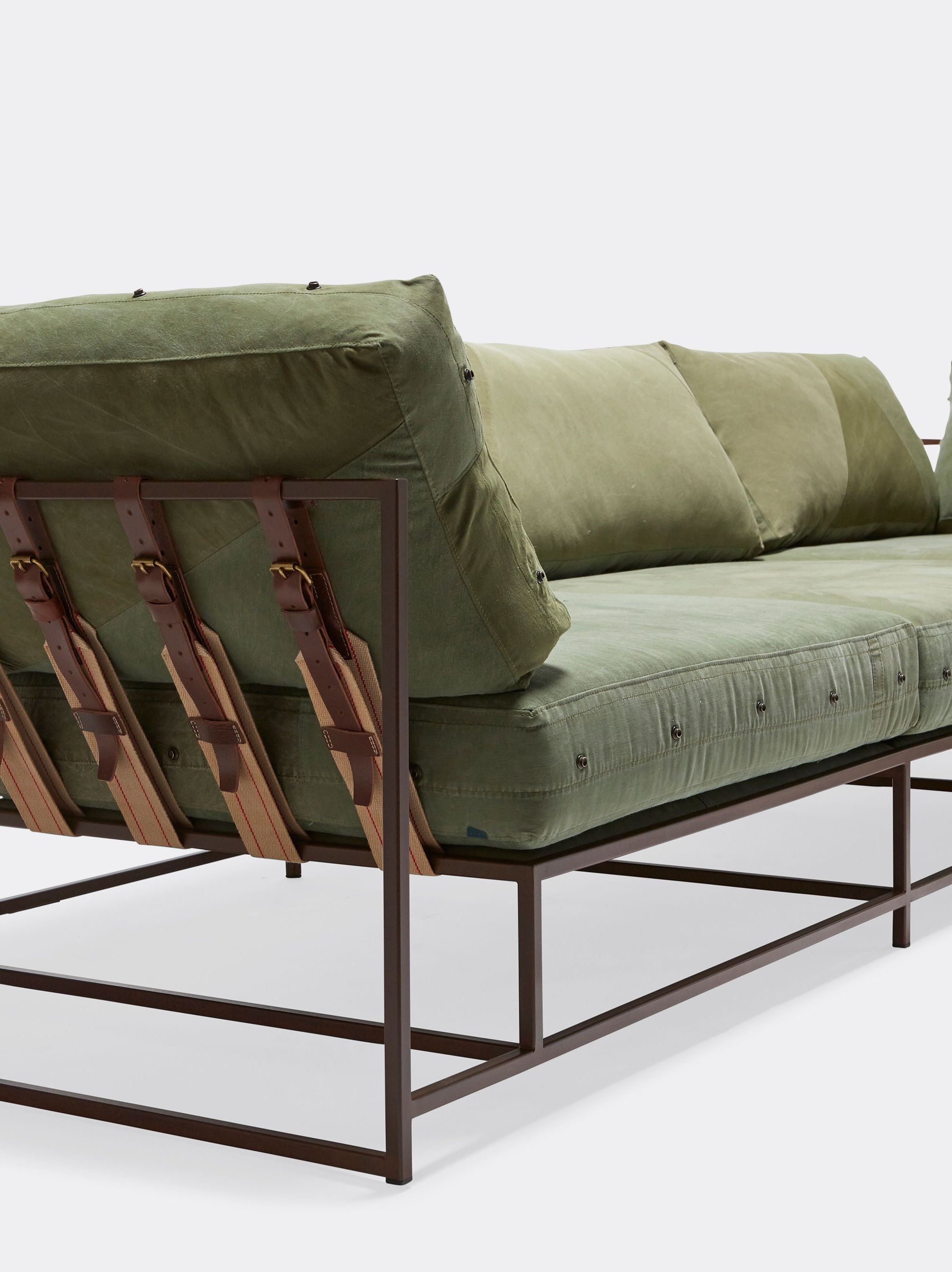 a green sectional sofa with a brown steel frame and leather and webbing supporting belts on a white background .