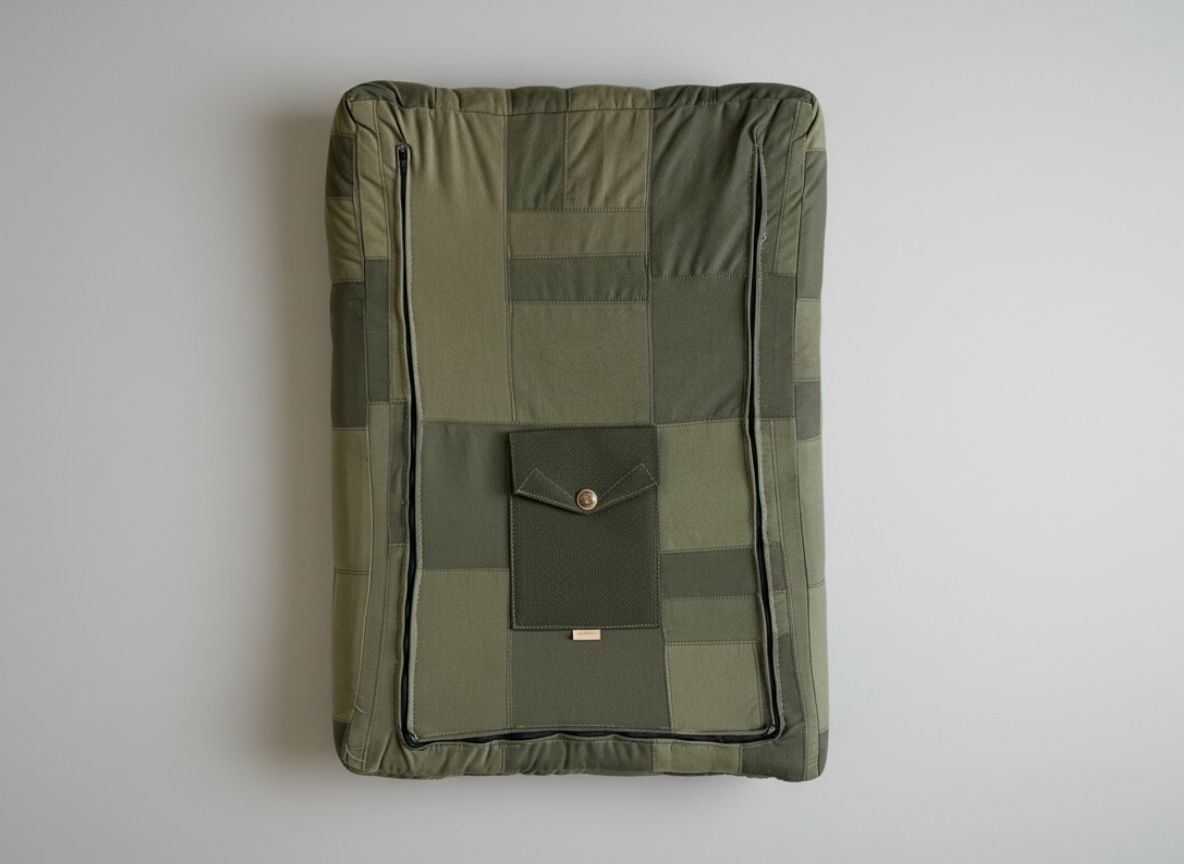 A rectangular green patchwork cushion with two vertical zippers and a central flap pocket secured by a brass button.
