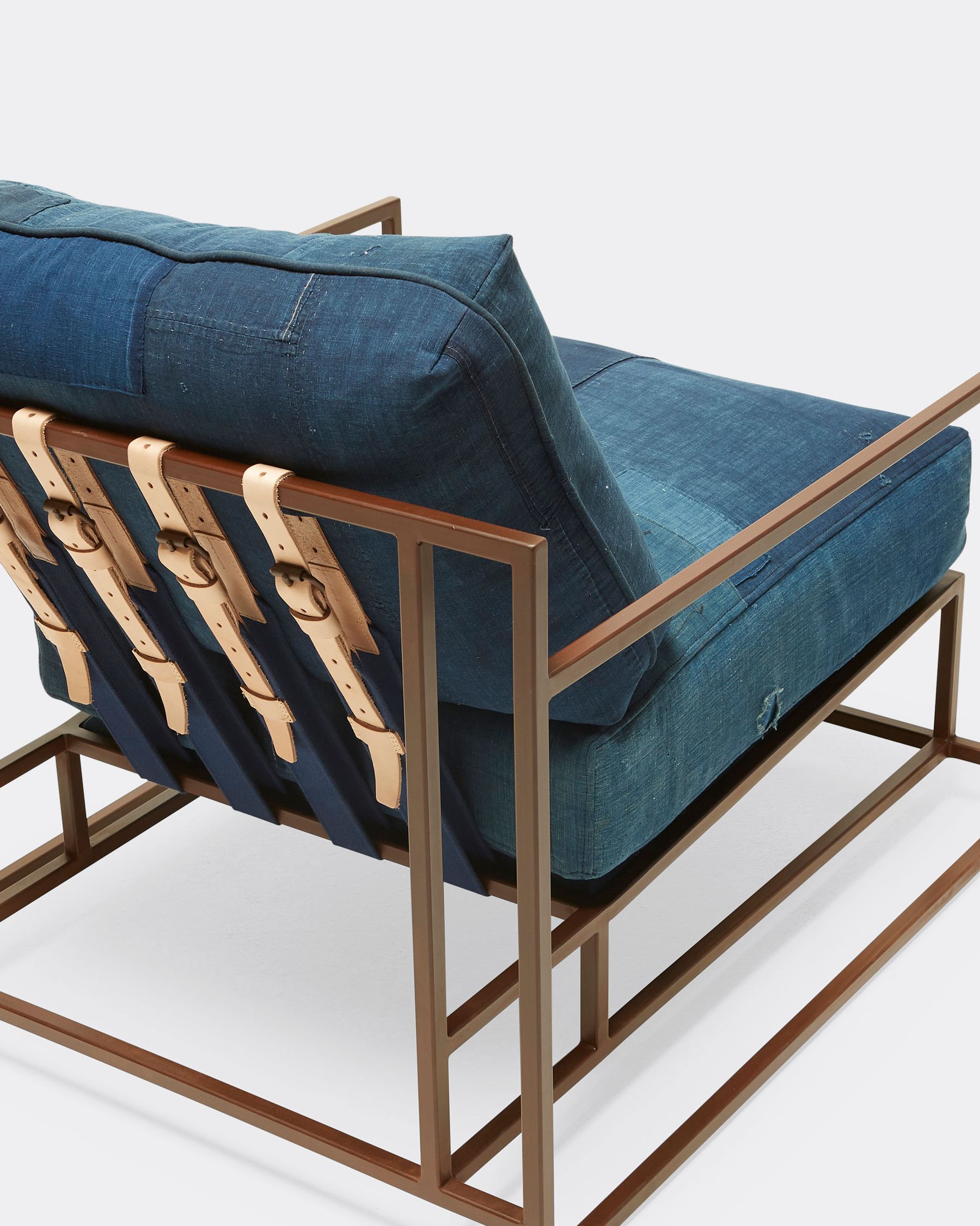 a steel framed chair finished in rust with vintage Japanese indigo cushions and leather and webbing supporting belts shown on a white background