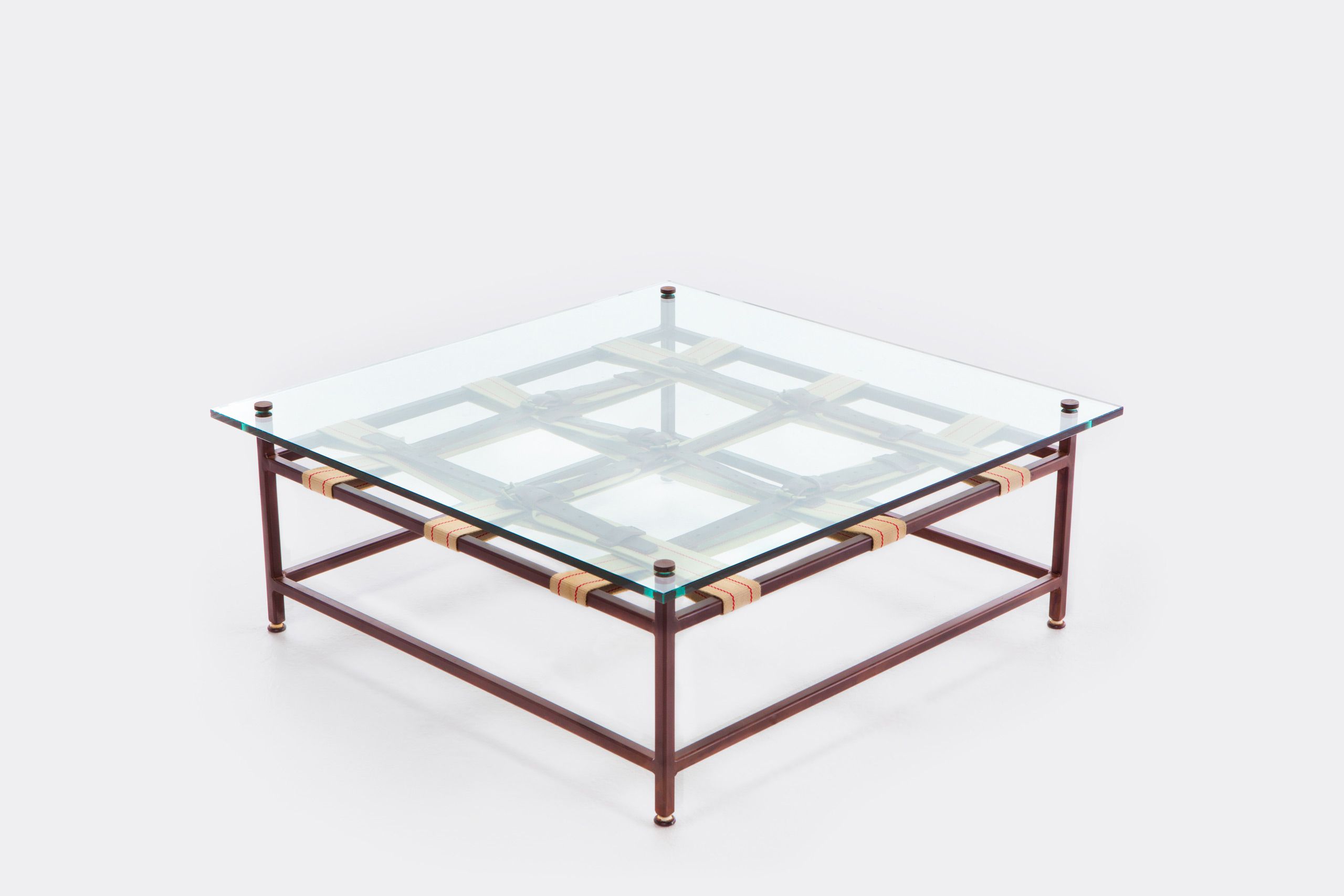 a coffee table with a glass top and a steel frame with decorative leather and webbing belts shown on a white background .