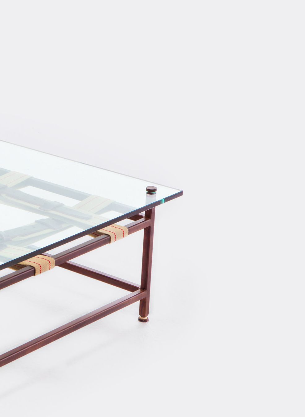 a coffee table with a glass top and a steel frame with decorative leather and webbing belts shown on a white background .