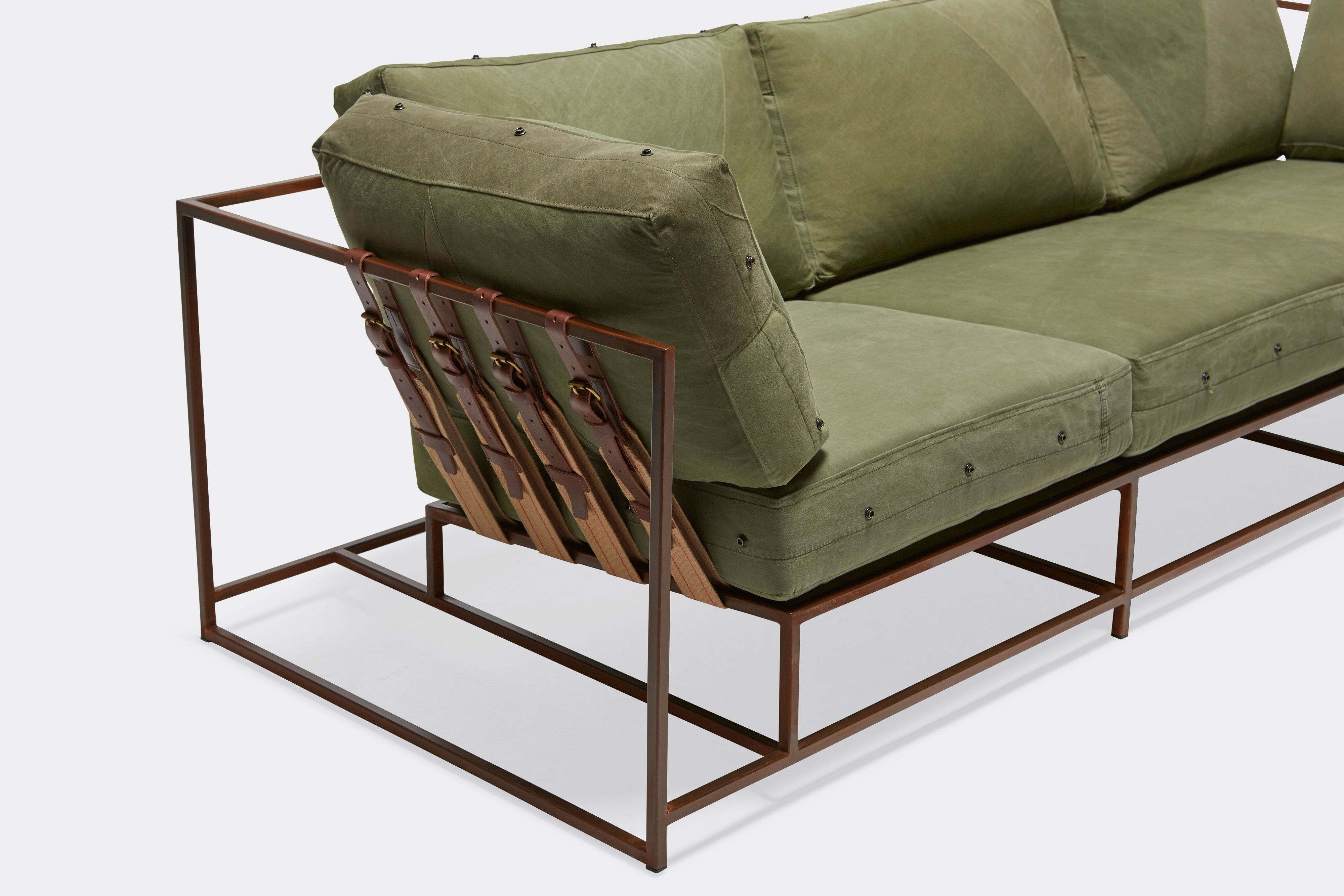 overhead of sofa with green canvas upholstery and brown belts on marbled rust metal frame