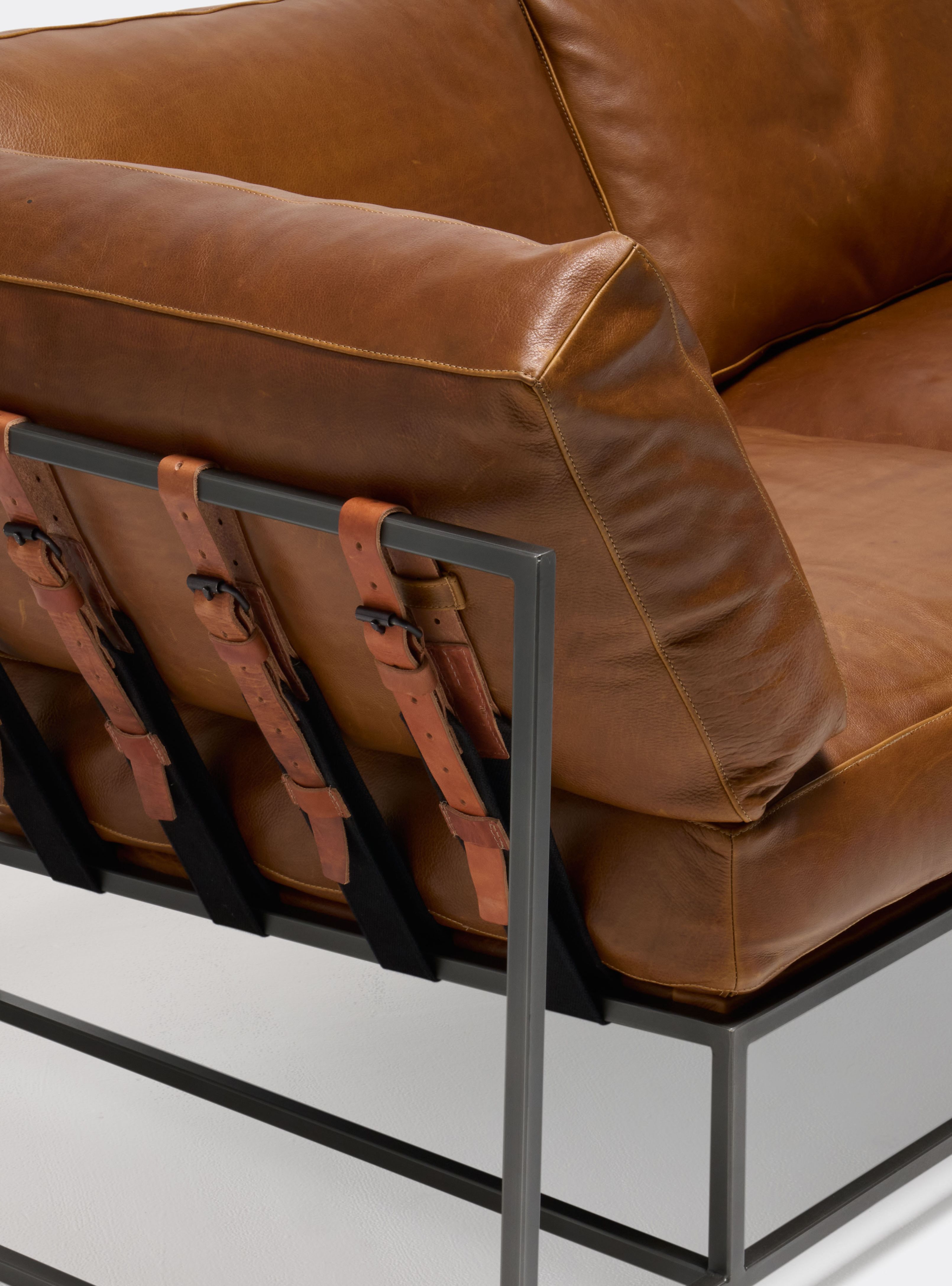 a brown leather couch with a metal frame and leather and webbing supporting belts shown on a white background .