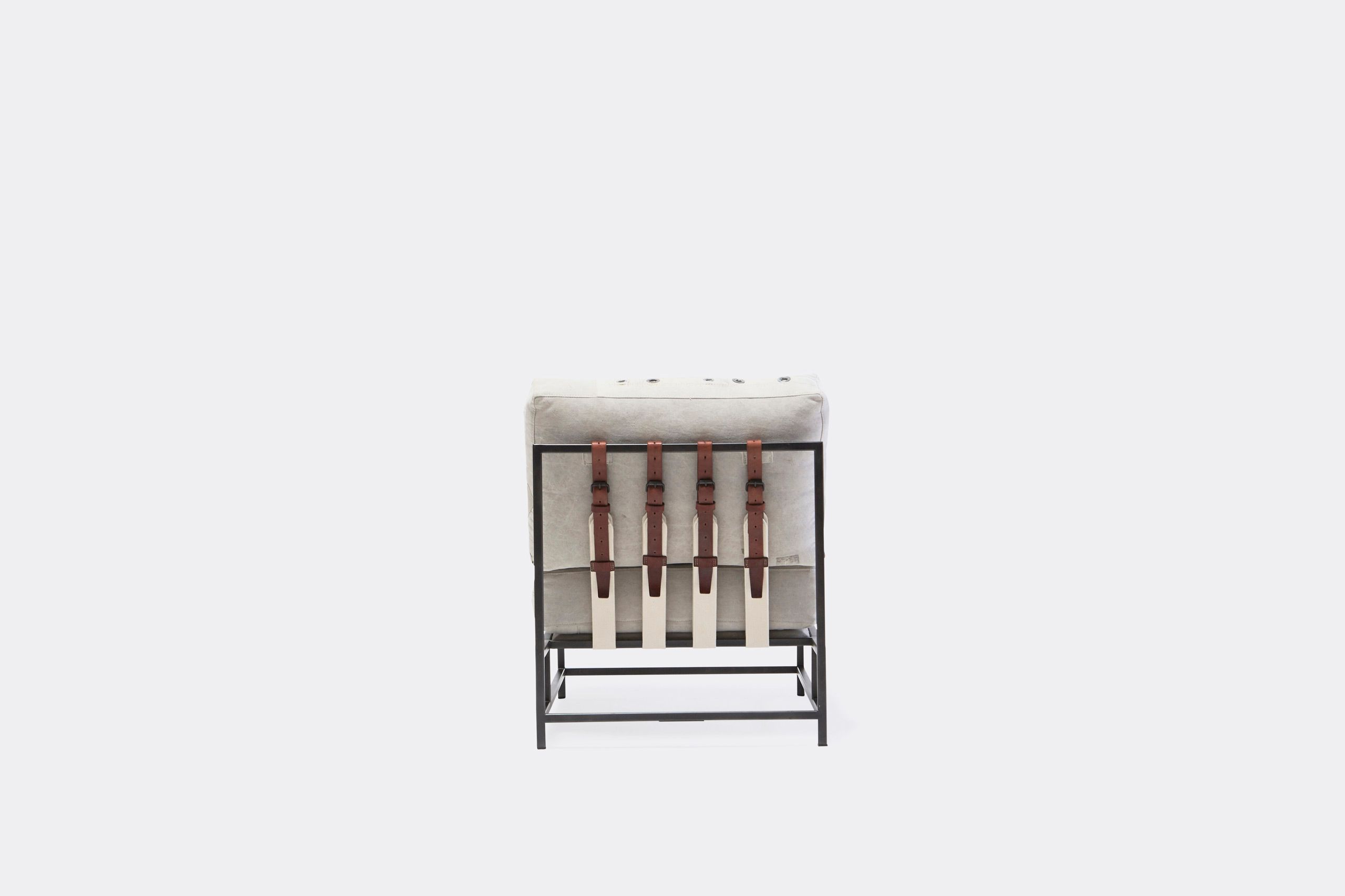 A chair with a white cushion and leather straps atop a blackened steel frame on a white background