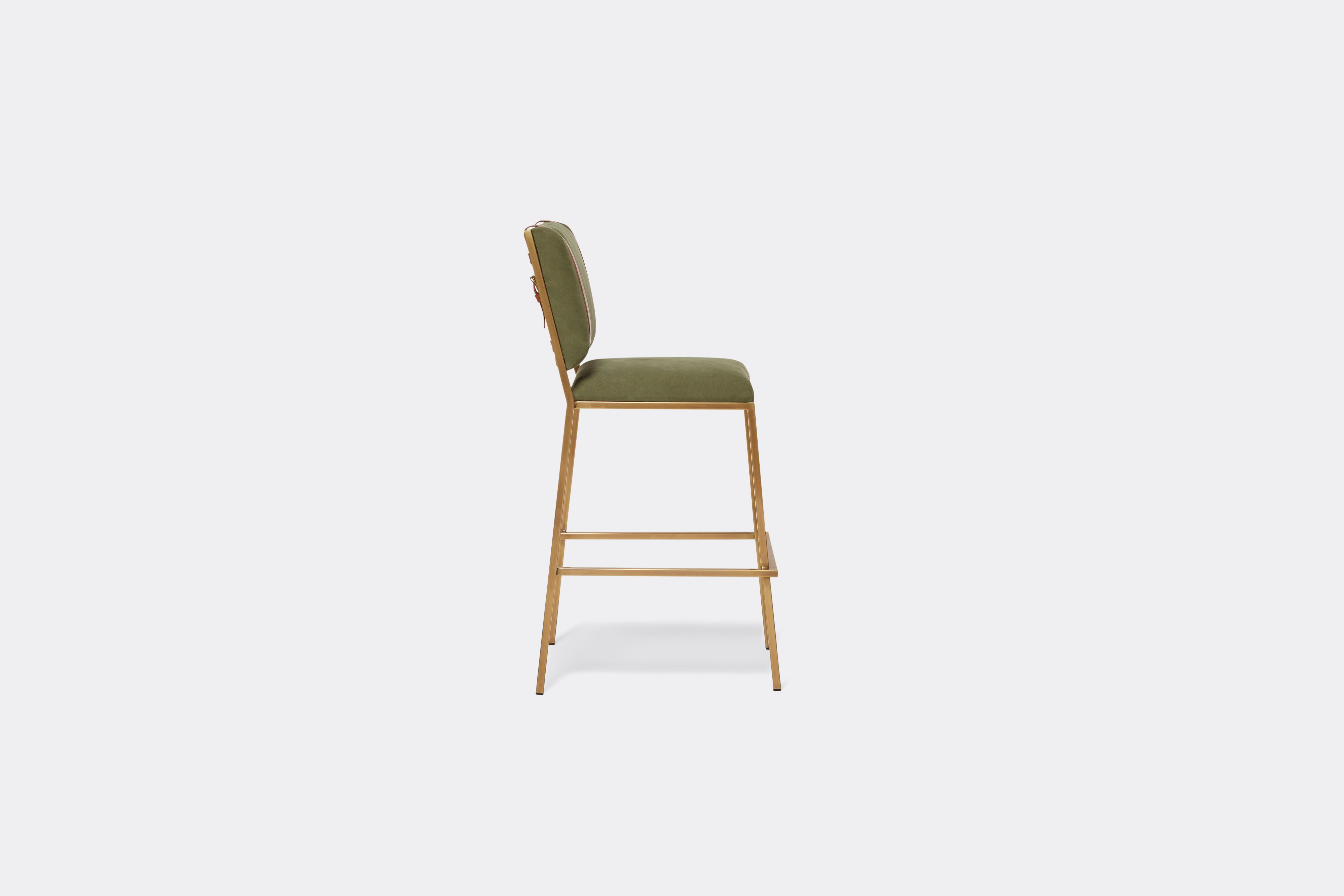 Sideview of barstool with military canvas upholstery and brown leather belts on antique brass metal legs