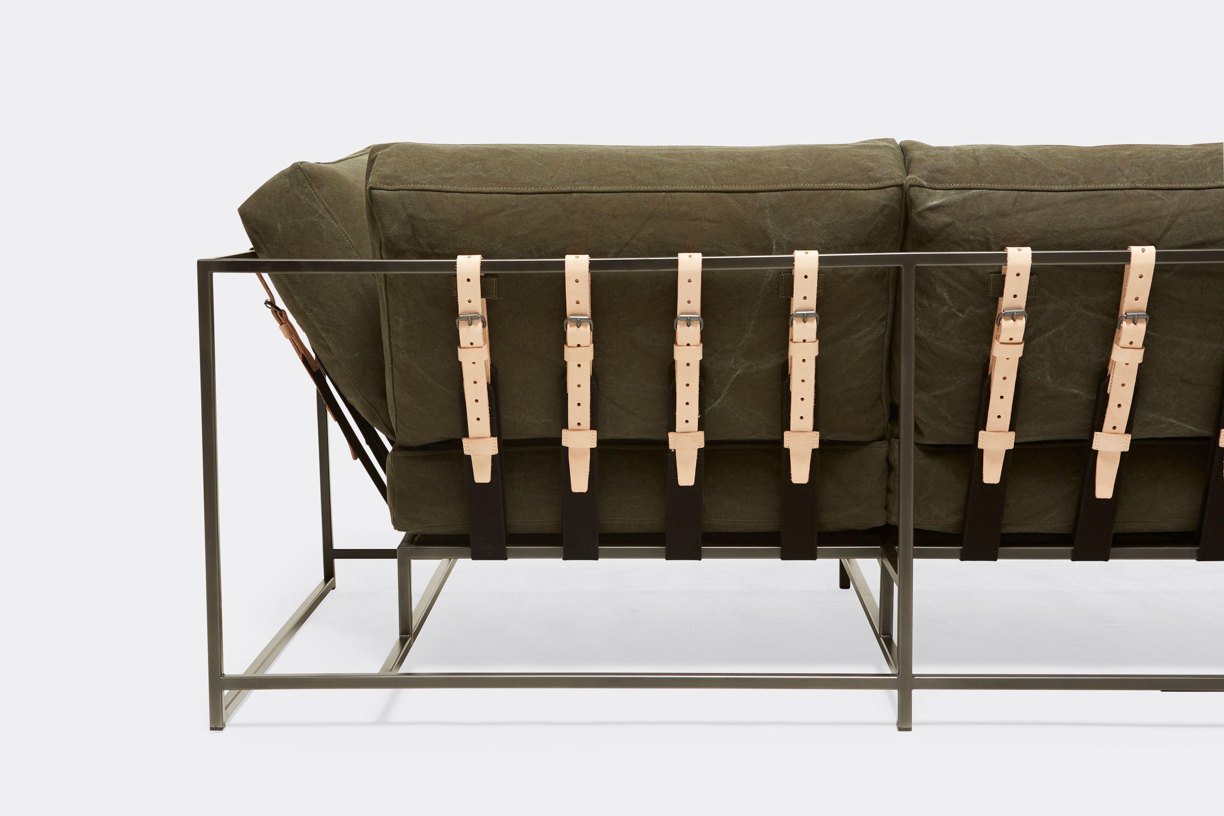 detail back of sofa with green canvas upholstery and natural leather belts on black metal frame