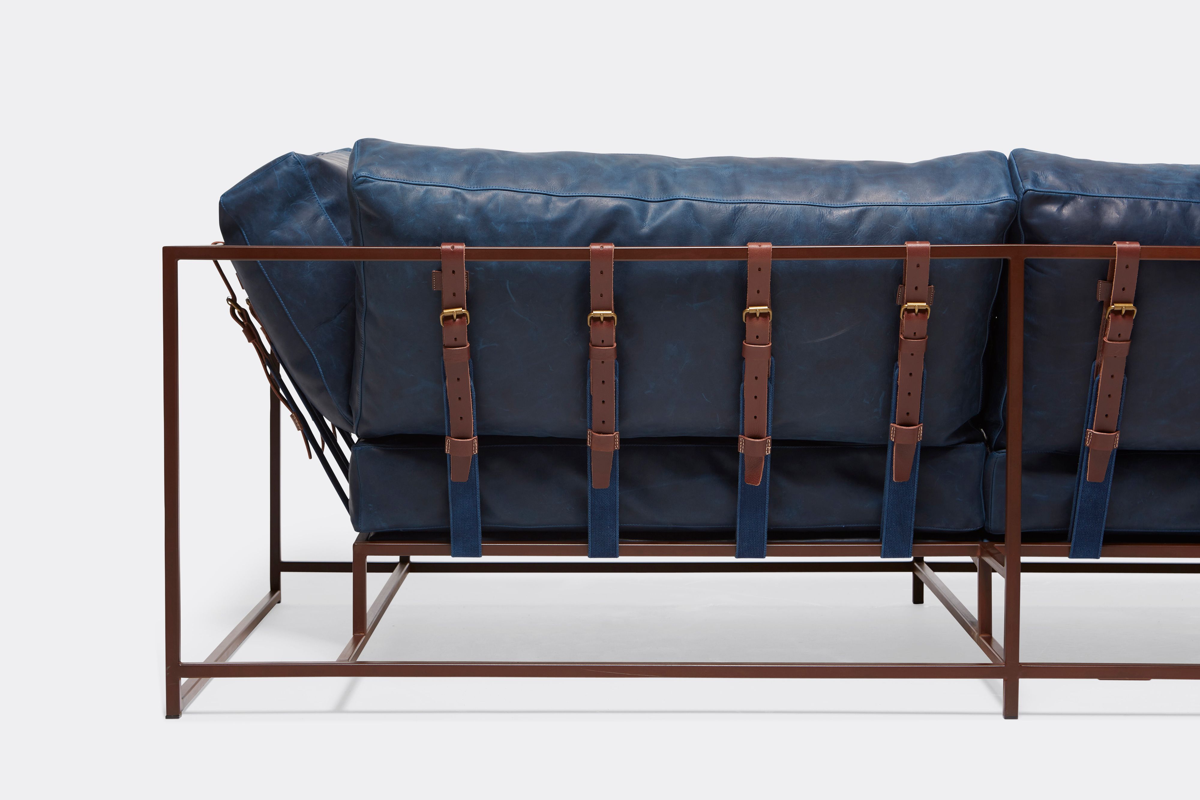 back of two seat sofa with blue leather upholstery and brown leather belts on marble rust metal frame
