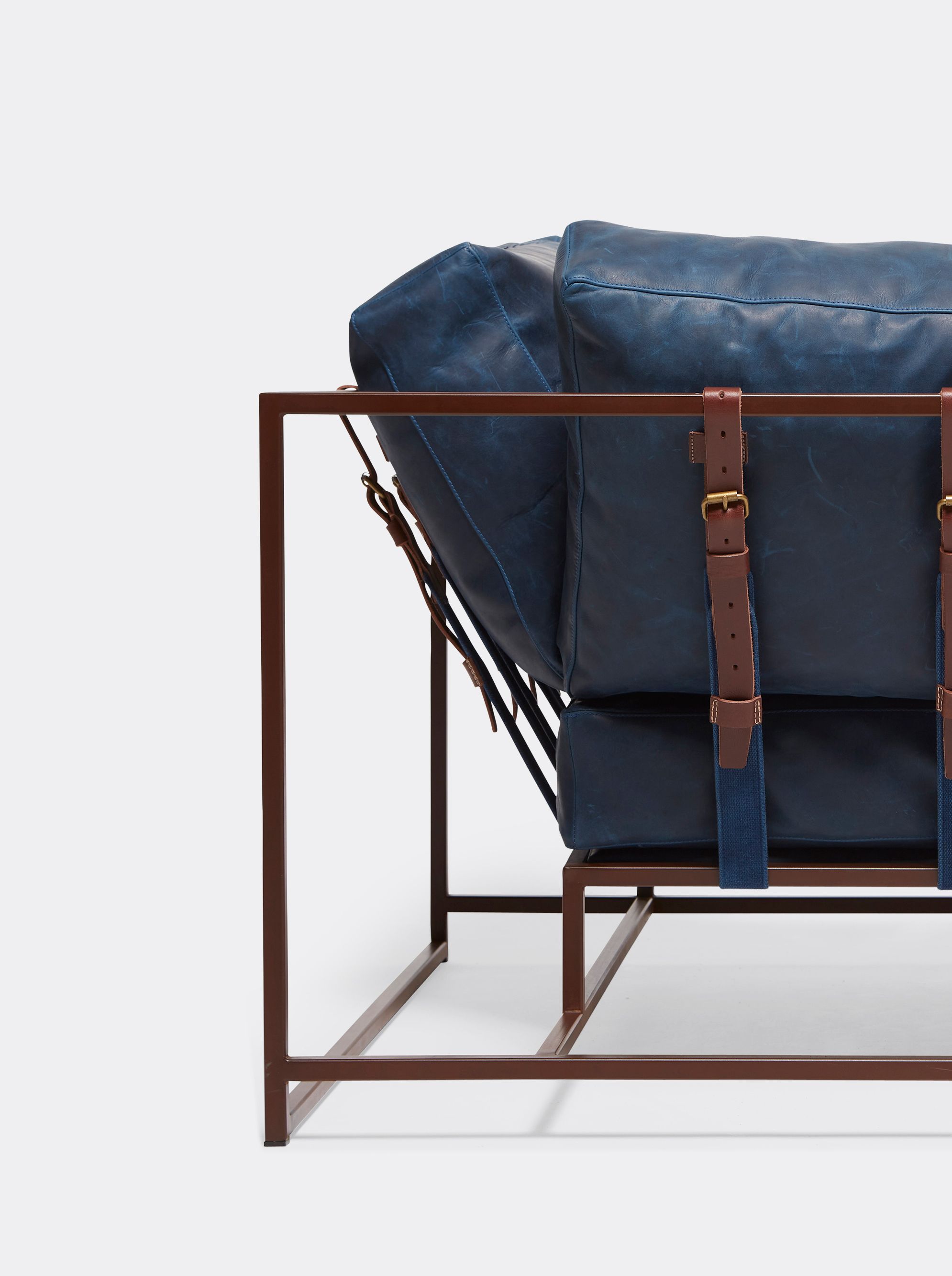 A navy blue leather couch with leather and webbing supporting belts and a rust finished steel frame shown on a white background .