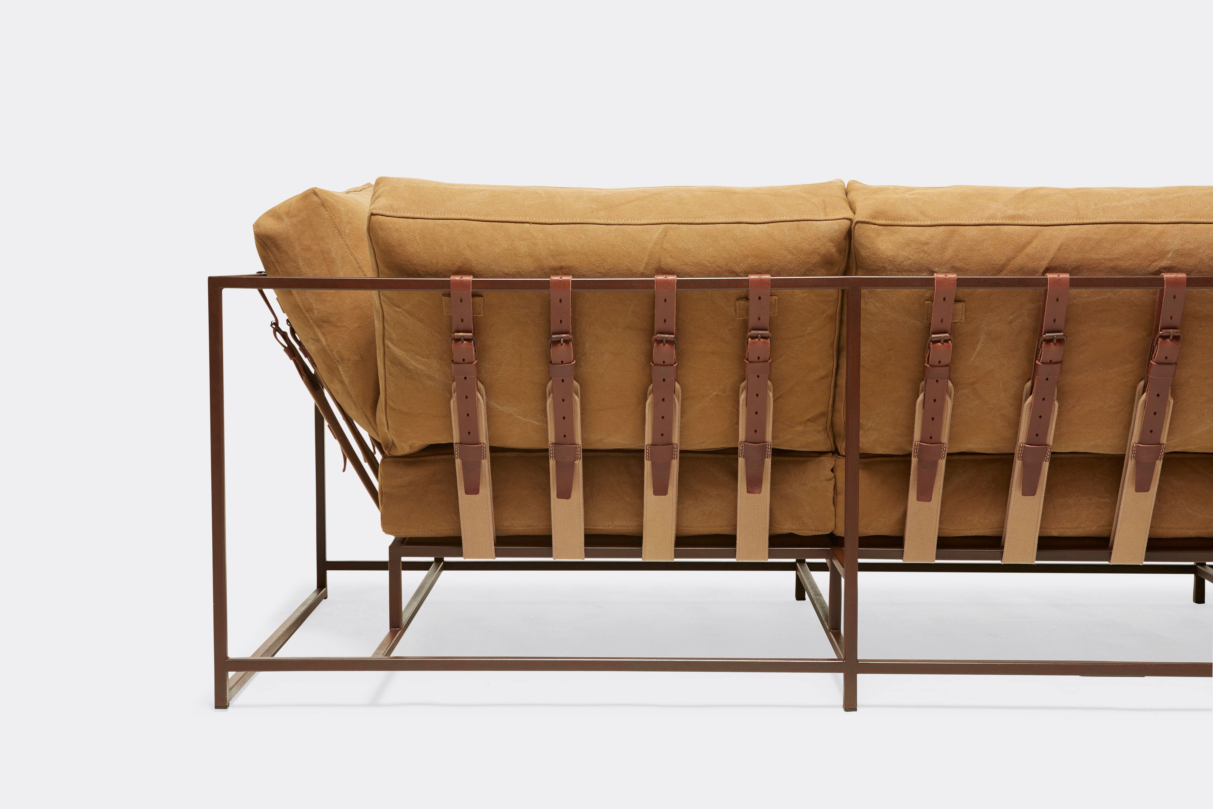 back detail of sofa with tan canvas upholstery and brown leather belts on marble rust metal frame
