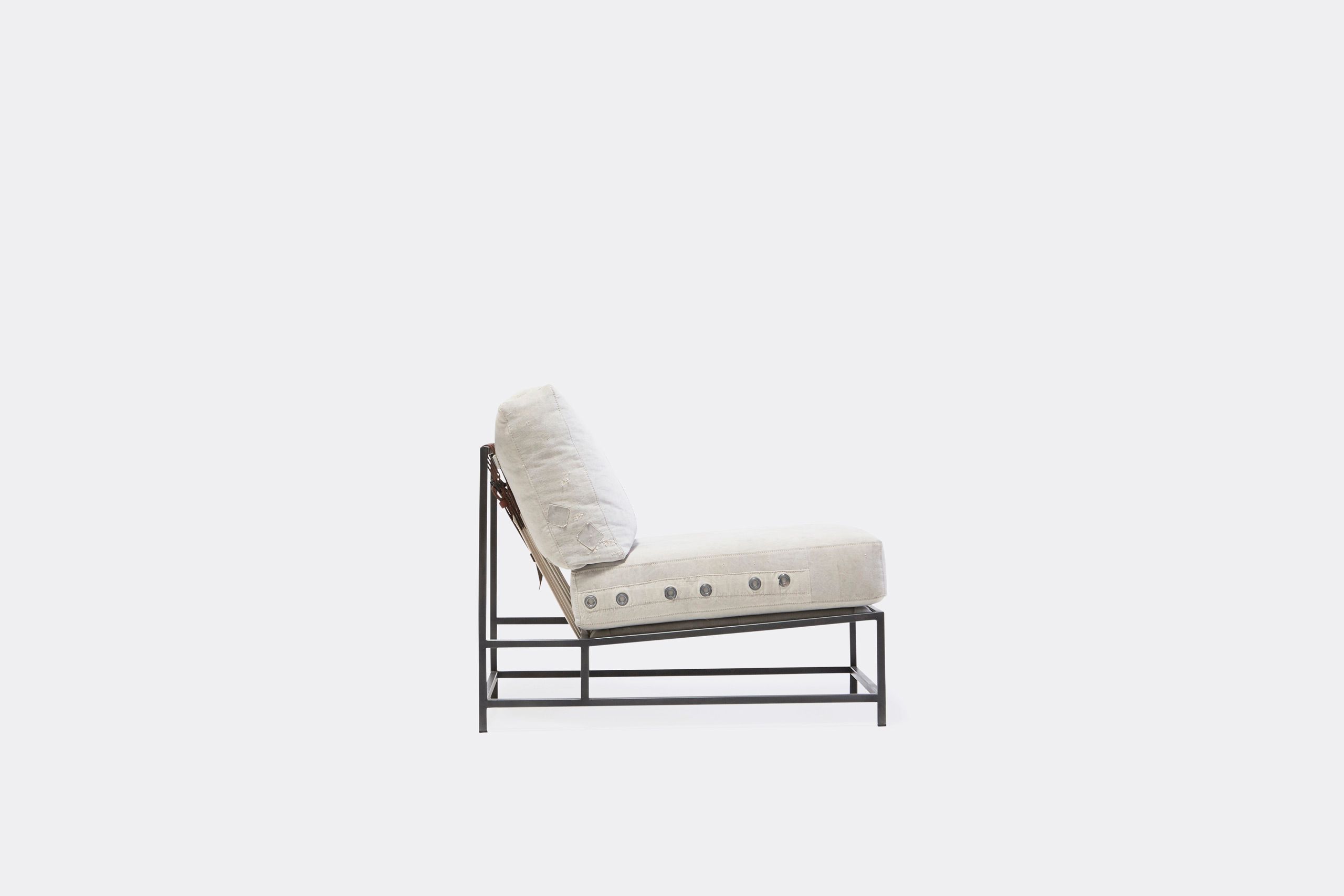A chair with a white cushion and leather straps atop a blackened steel frame on a white background
