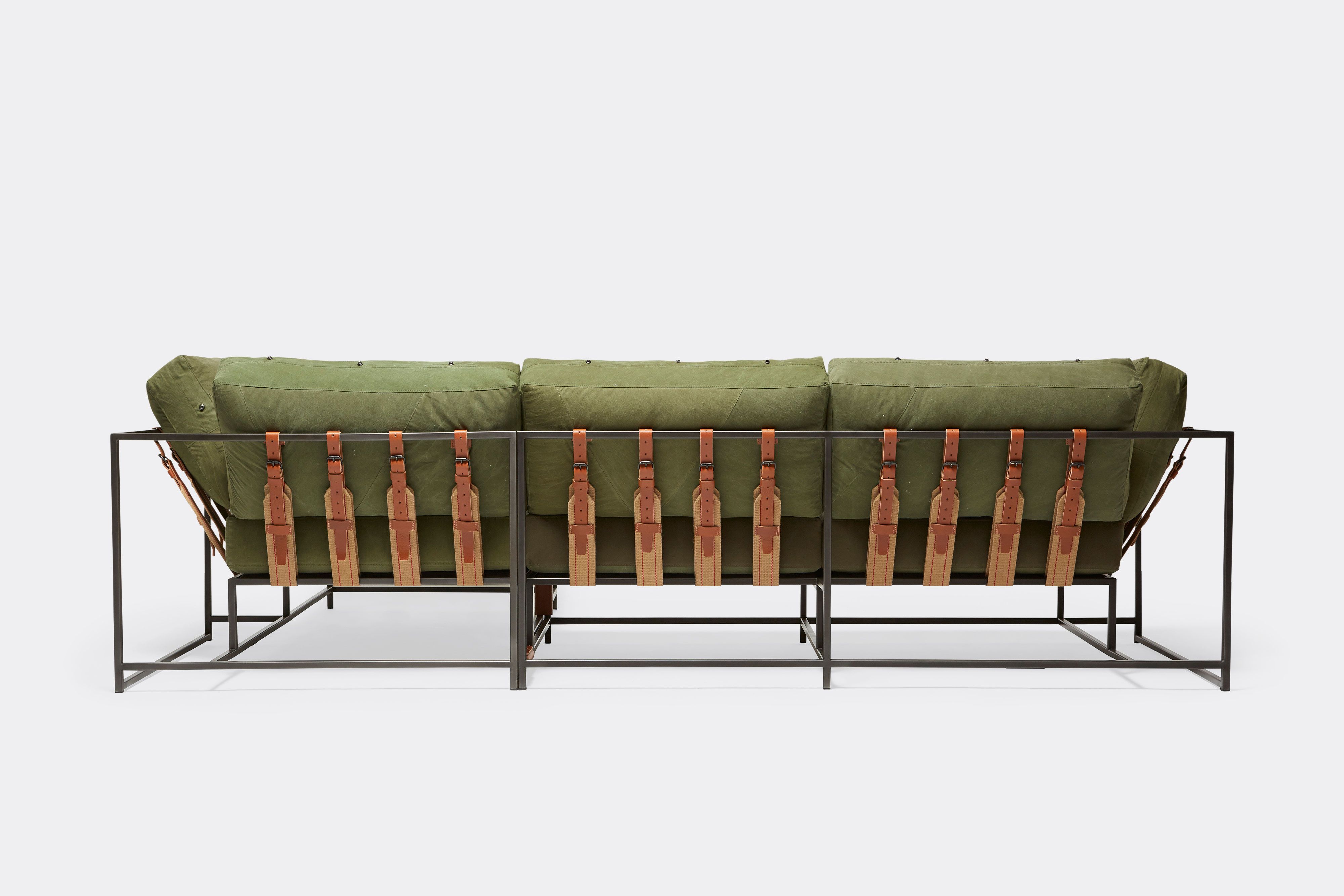 back of sectional with green canvas upholstery and brown leather belts on black metal frame