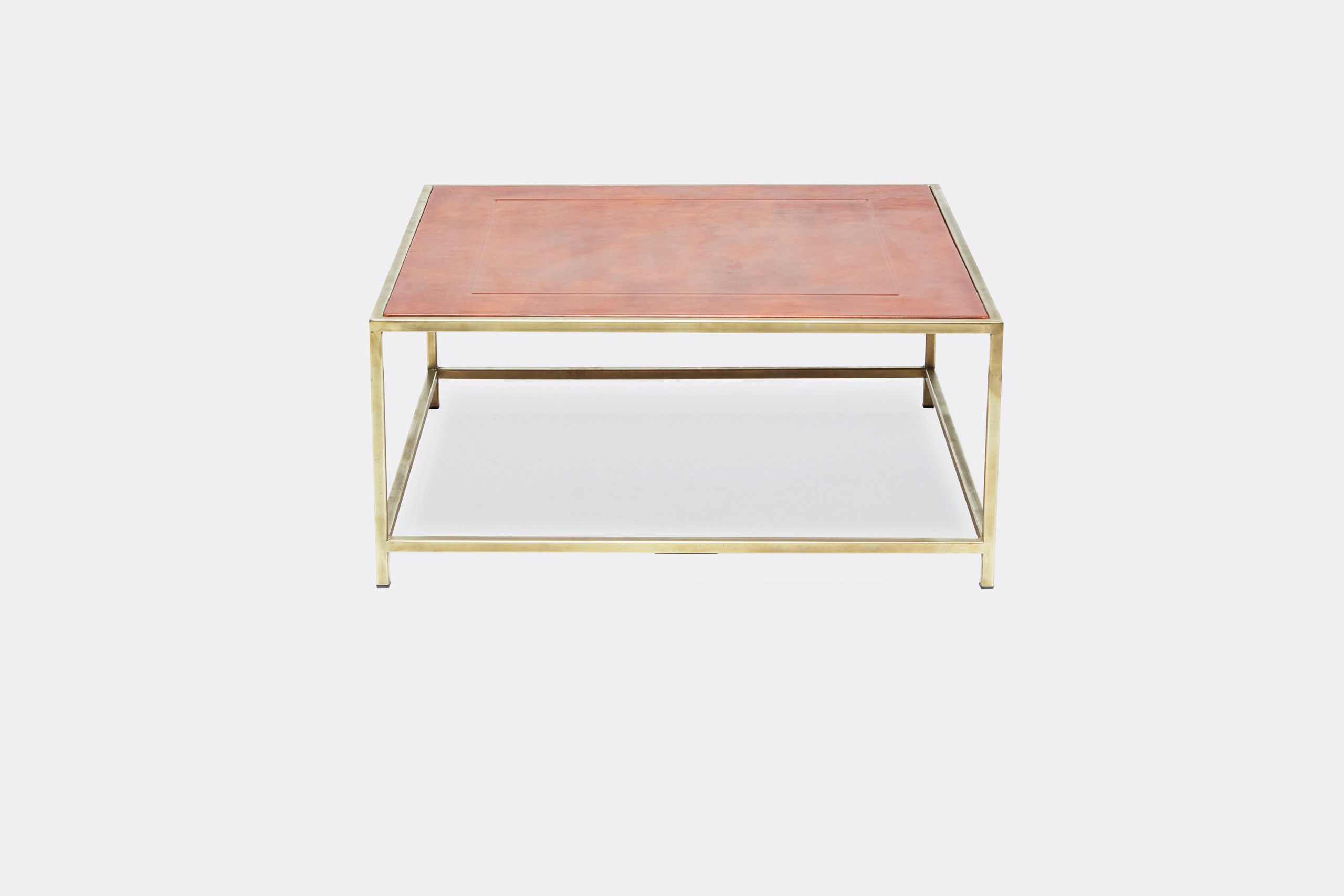 a square coffee table with a leather top and a brass frame on a white background .