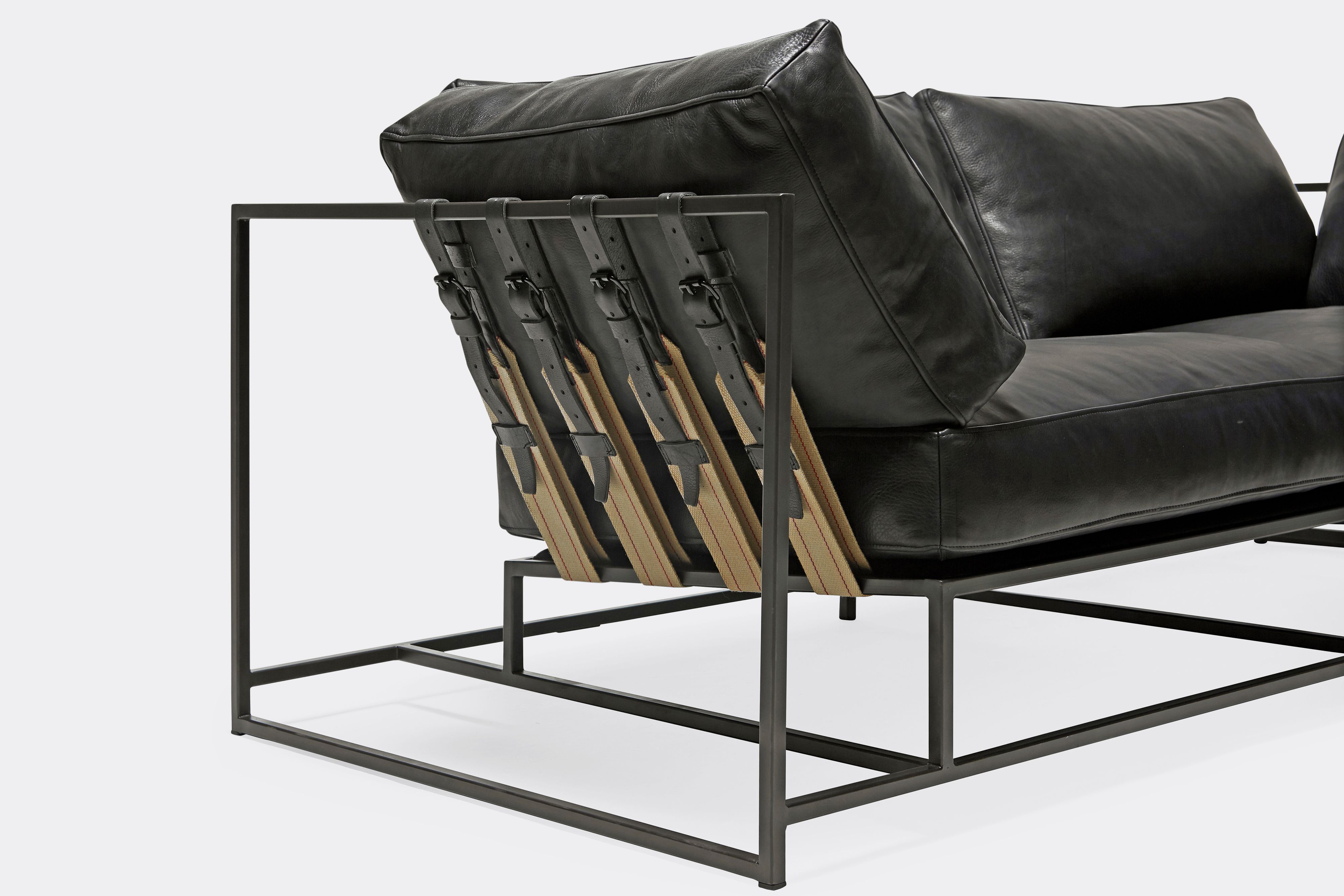 side detail of two seat sofa black leather upholstery and black leather belts on black metal frame
