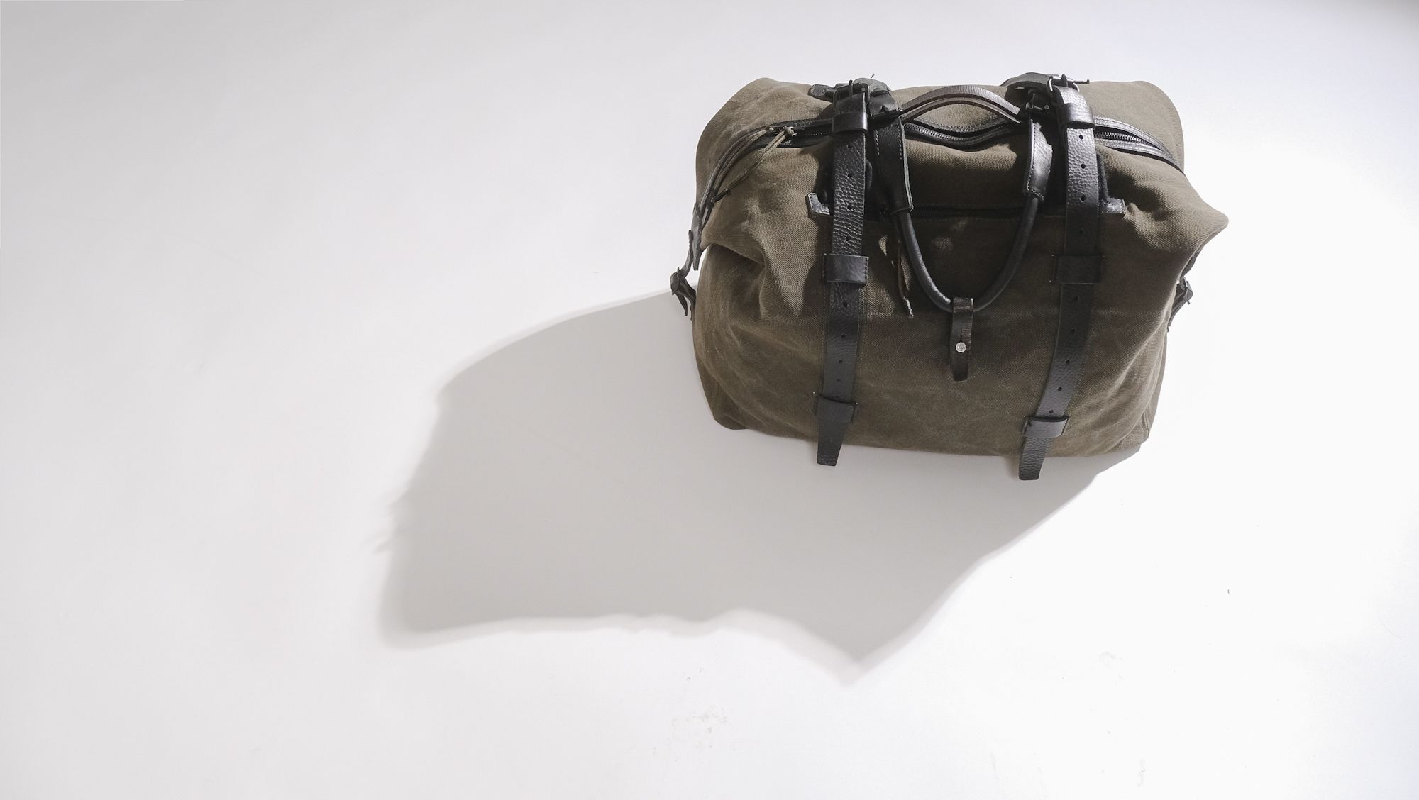 a brown duffel bag with black straps is sitting on a white surface .