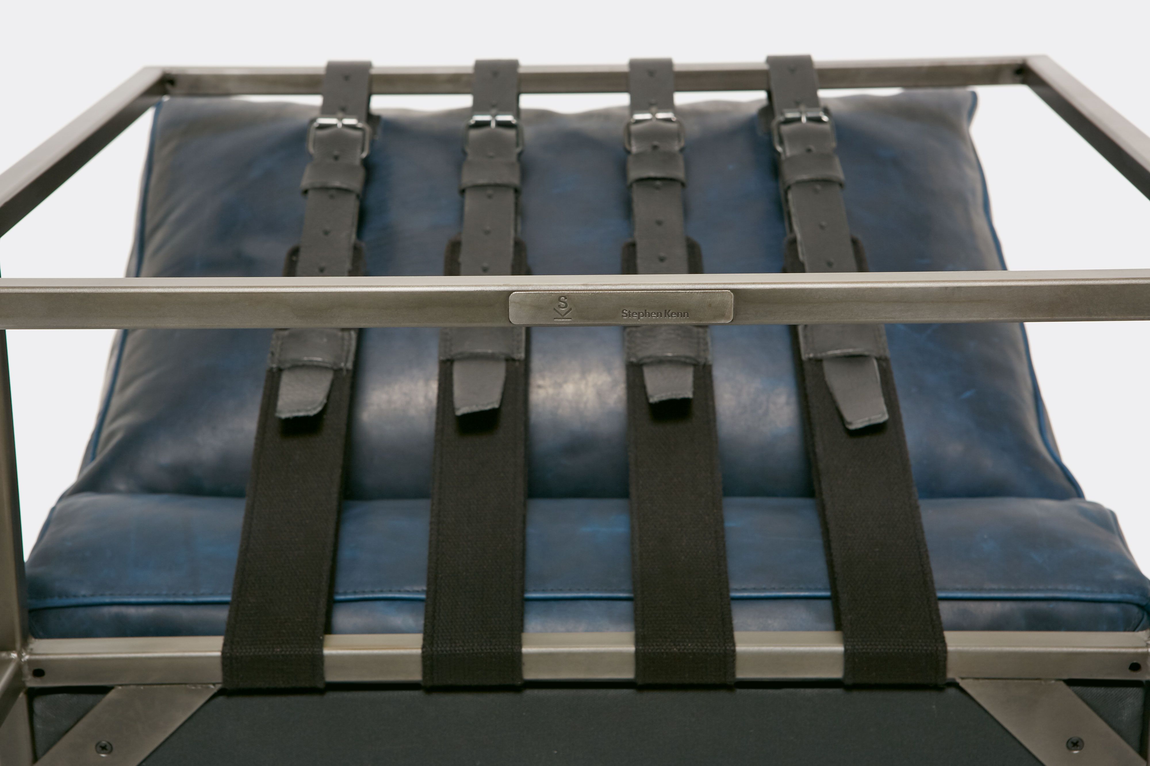 detail of lounge chair  with blue leather upholstery and black leather belts on antique nickel metal frame