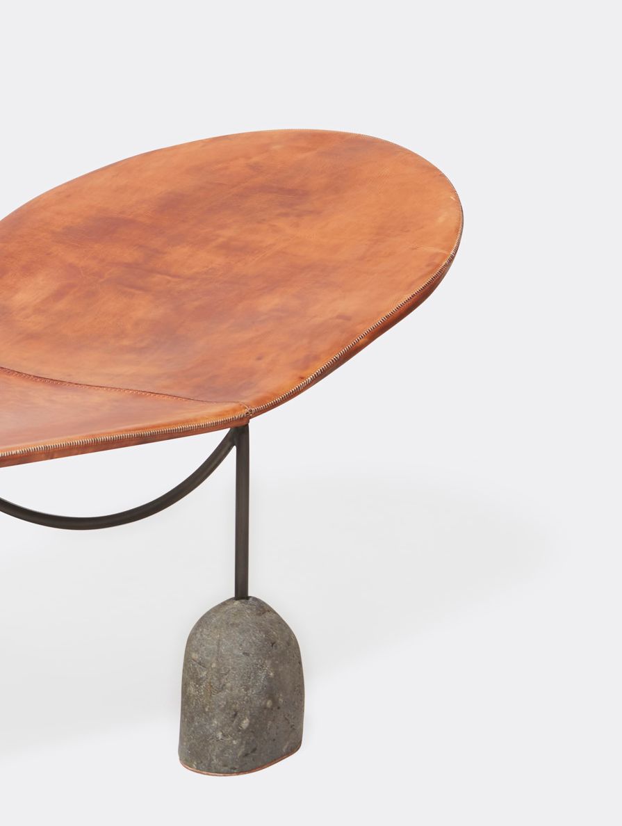 a brown leather chaise lounge with a steel frame and stone base shown on a white background .