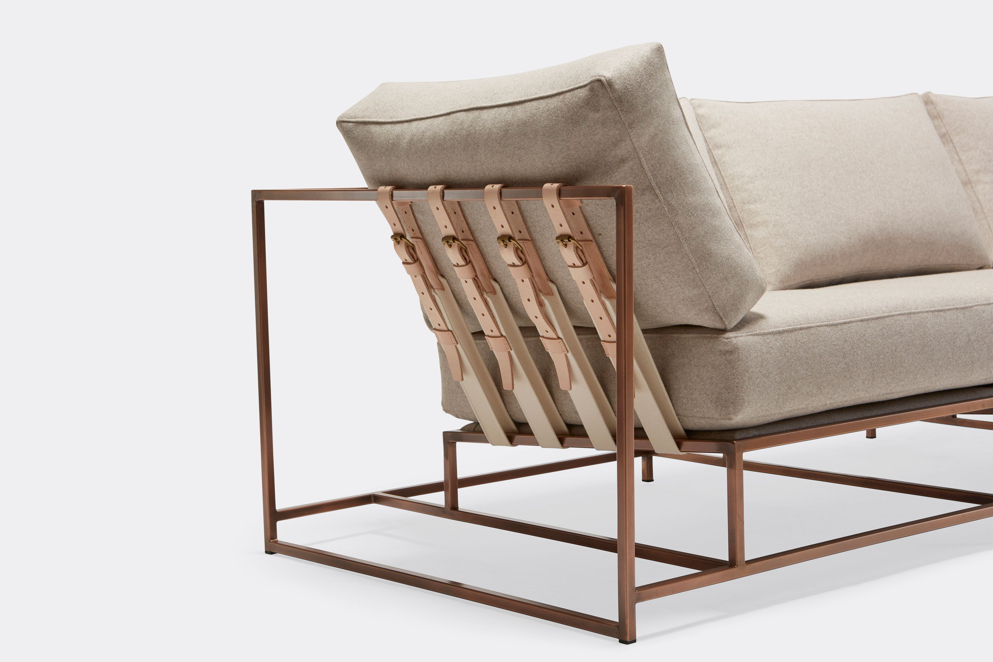side detail of three piece sofa with cream wool upholstery and natural tan leather belts on antique copper metal frame