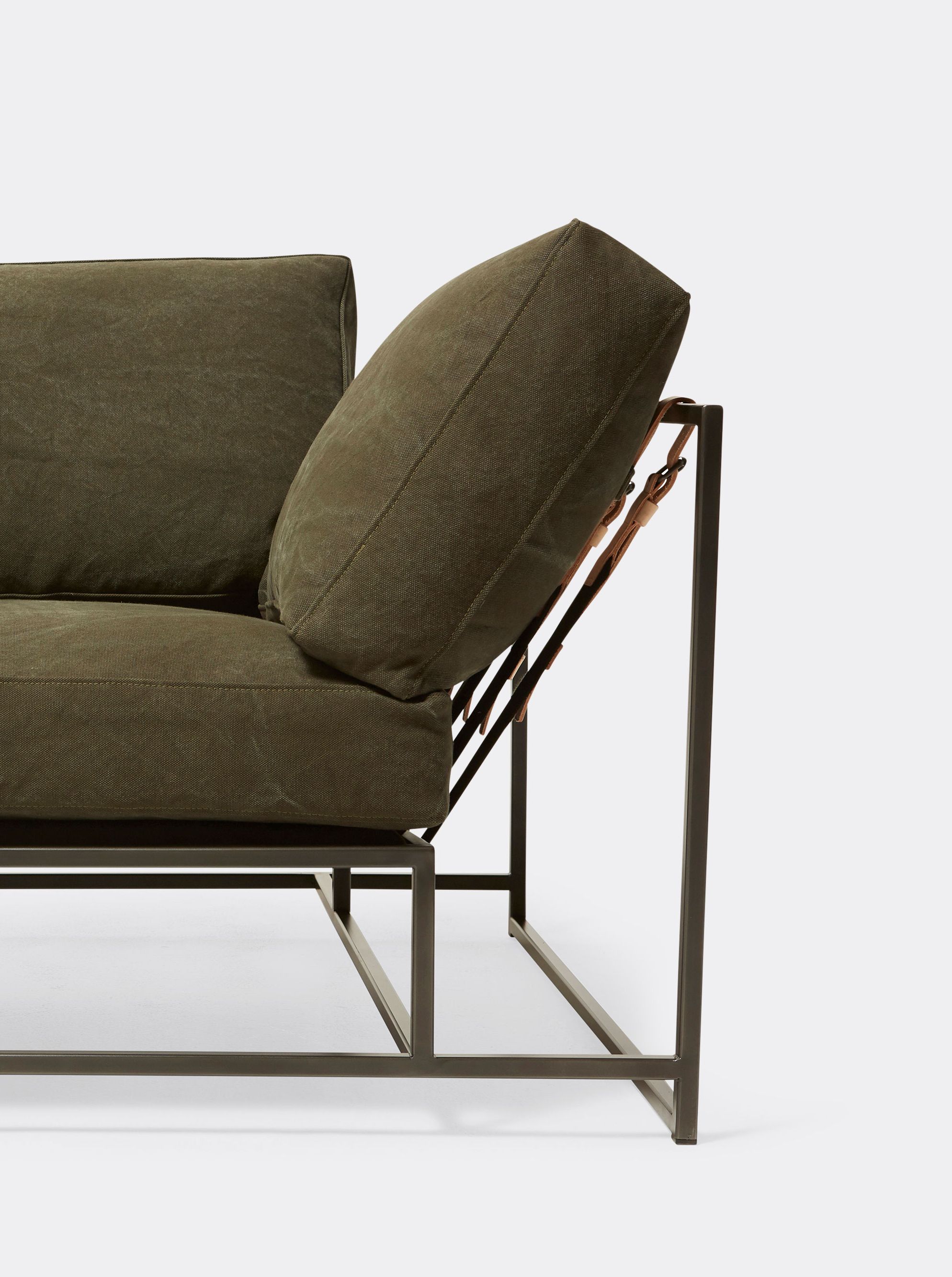 a green canvas sofa with a blackened steel frame and supporting belts on a white background .