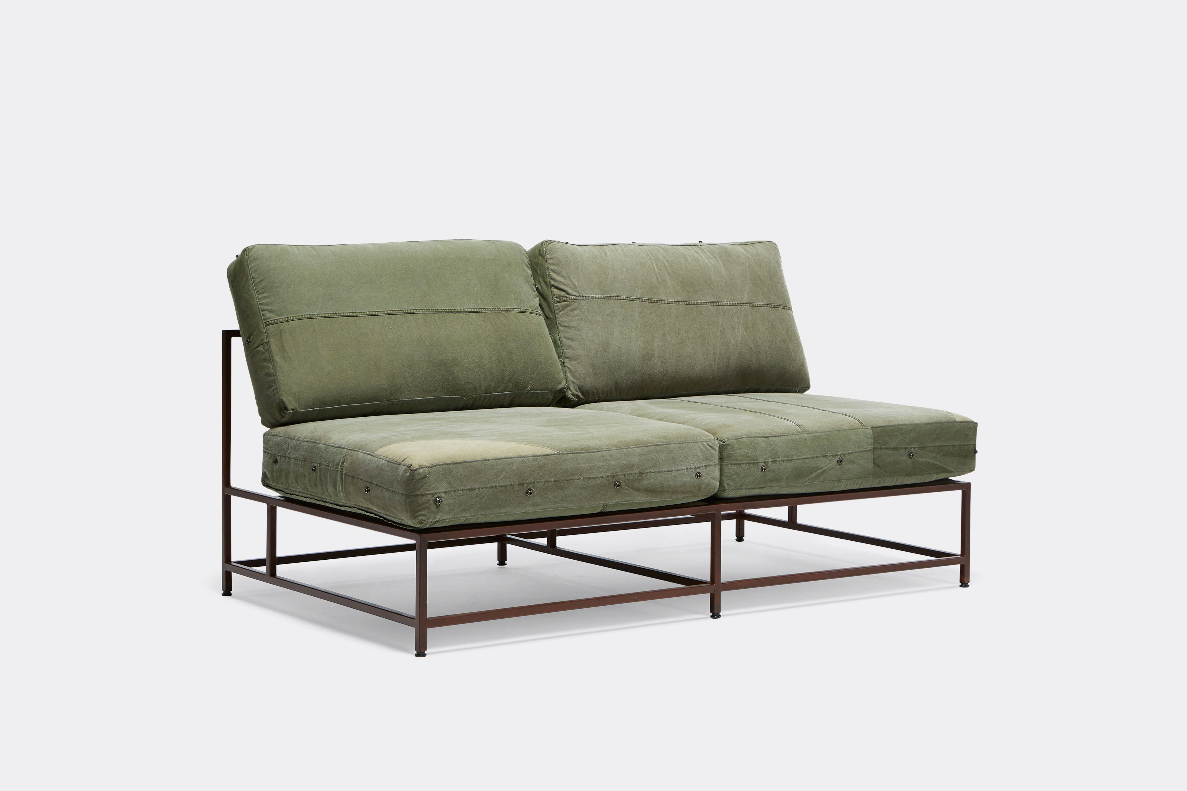 a steel framed loveseat sofa with green canvas cushions and leather and webbing supporting belts shown on a white background .