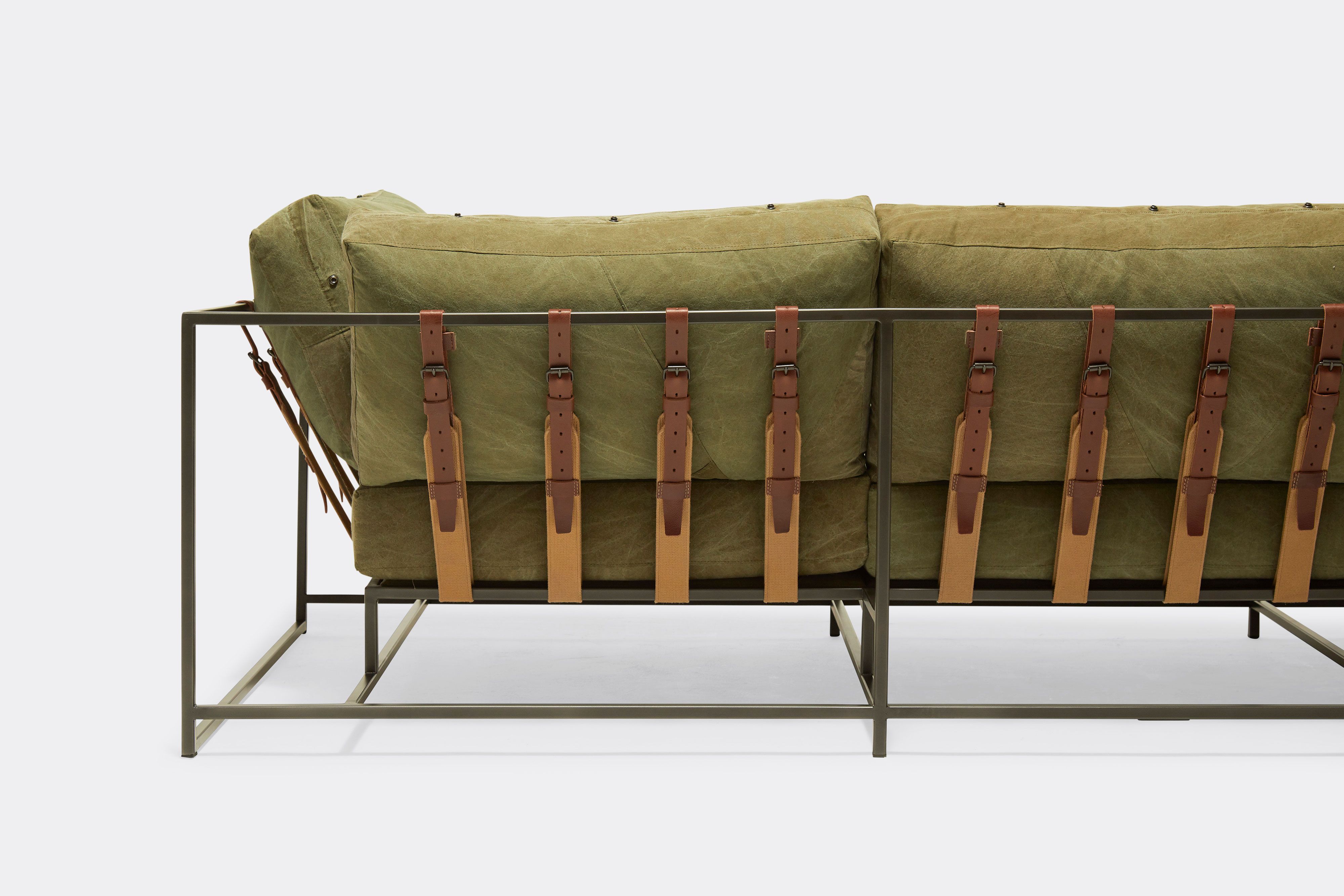 back detail of sofa with green canvas upholstery and brown belts on black metal frame