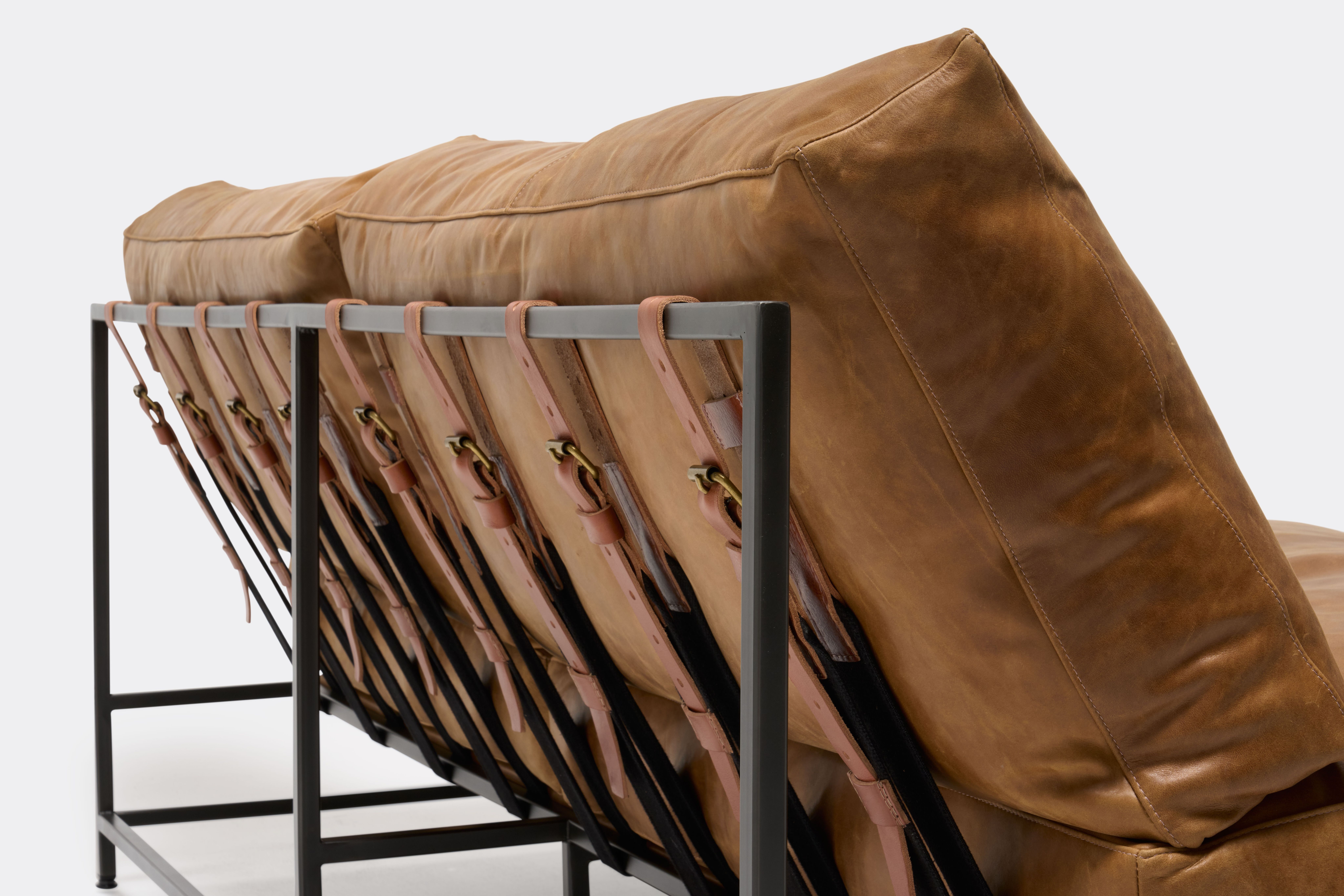 detail of loveseat with brown leather upholstery and brown leather belts on black metal frame