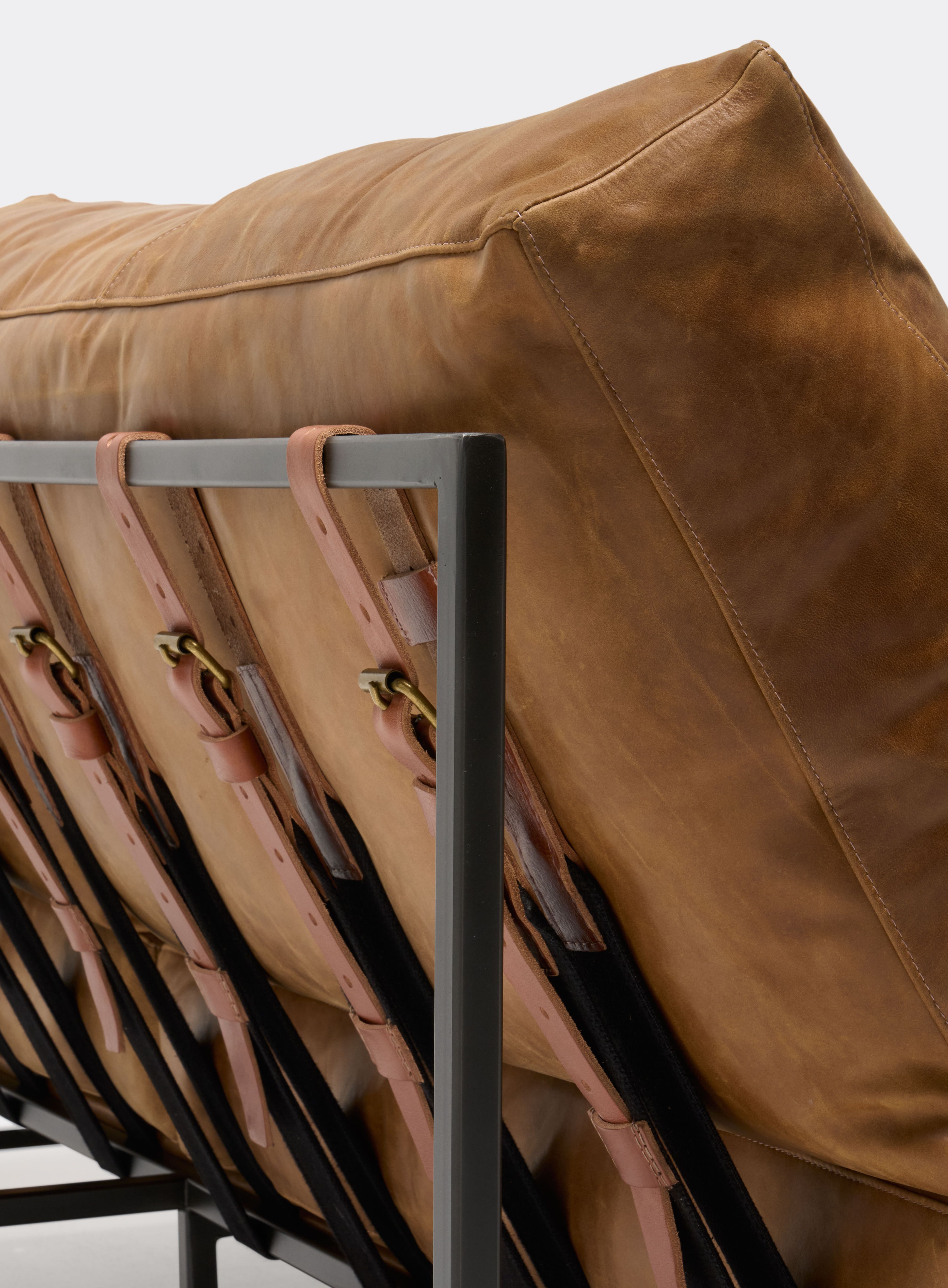 a brown leather couch with a black metal frame and leather and webbing supporting belts shown on a white background .