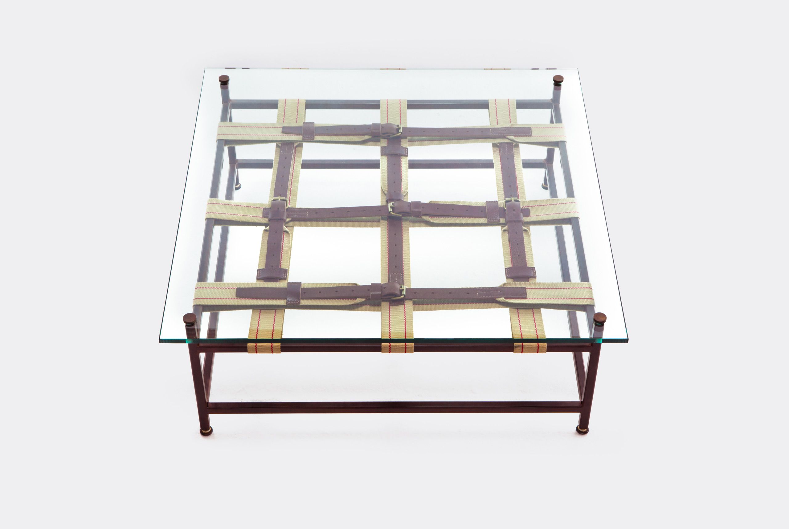 a coffee table with a glass top and a steel frame with decorative leather and webbing belts shown on a white background .