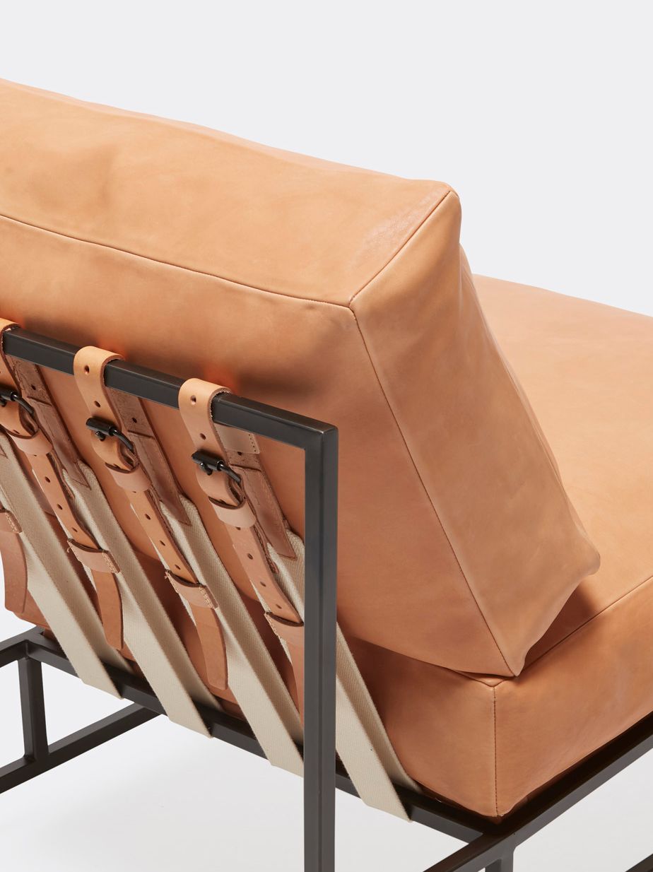 a tan leather chair with a metal frame and leather and webbing supporting belts shown on a white background .