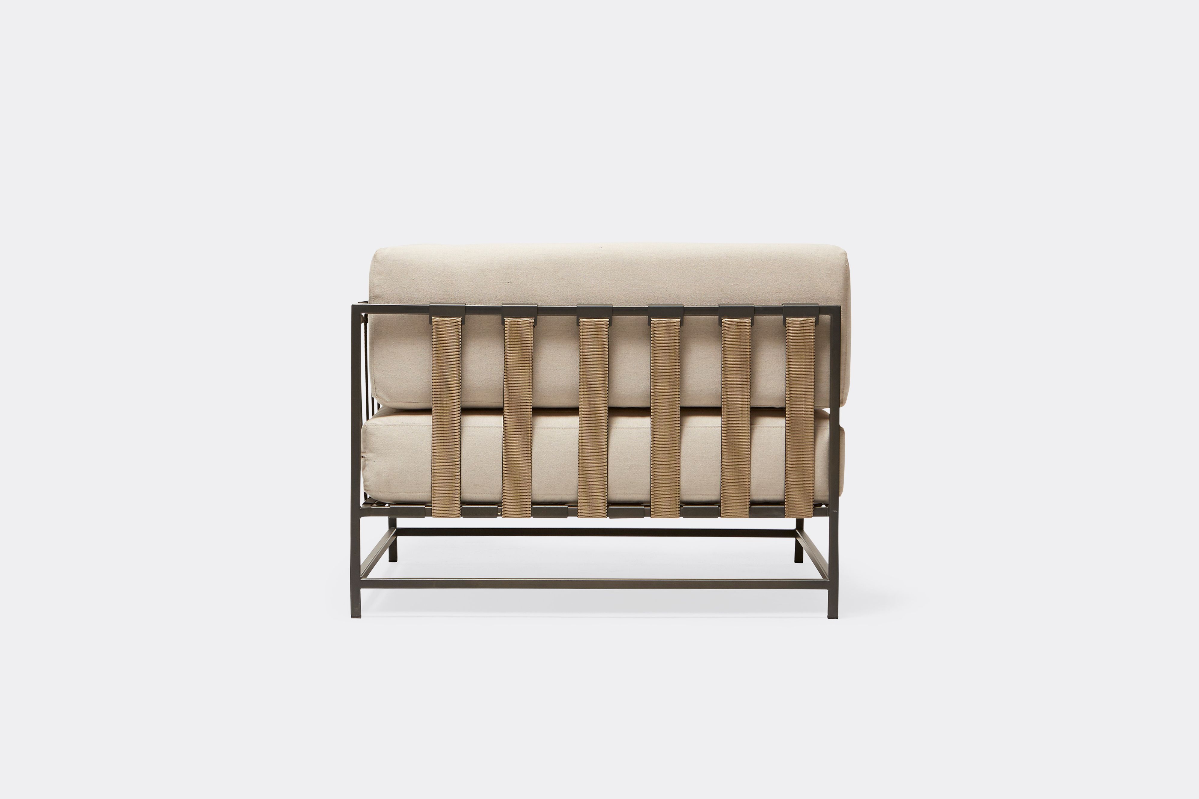 side of outdoor corner chair with cream canvas upholstery and tan belts on dark grey metal frame