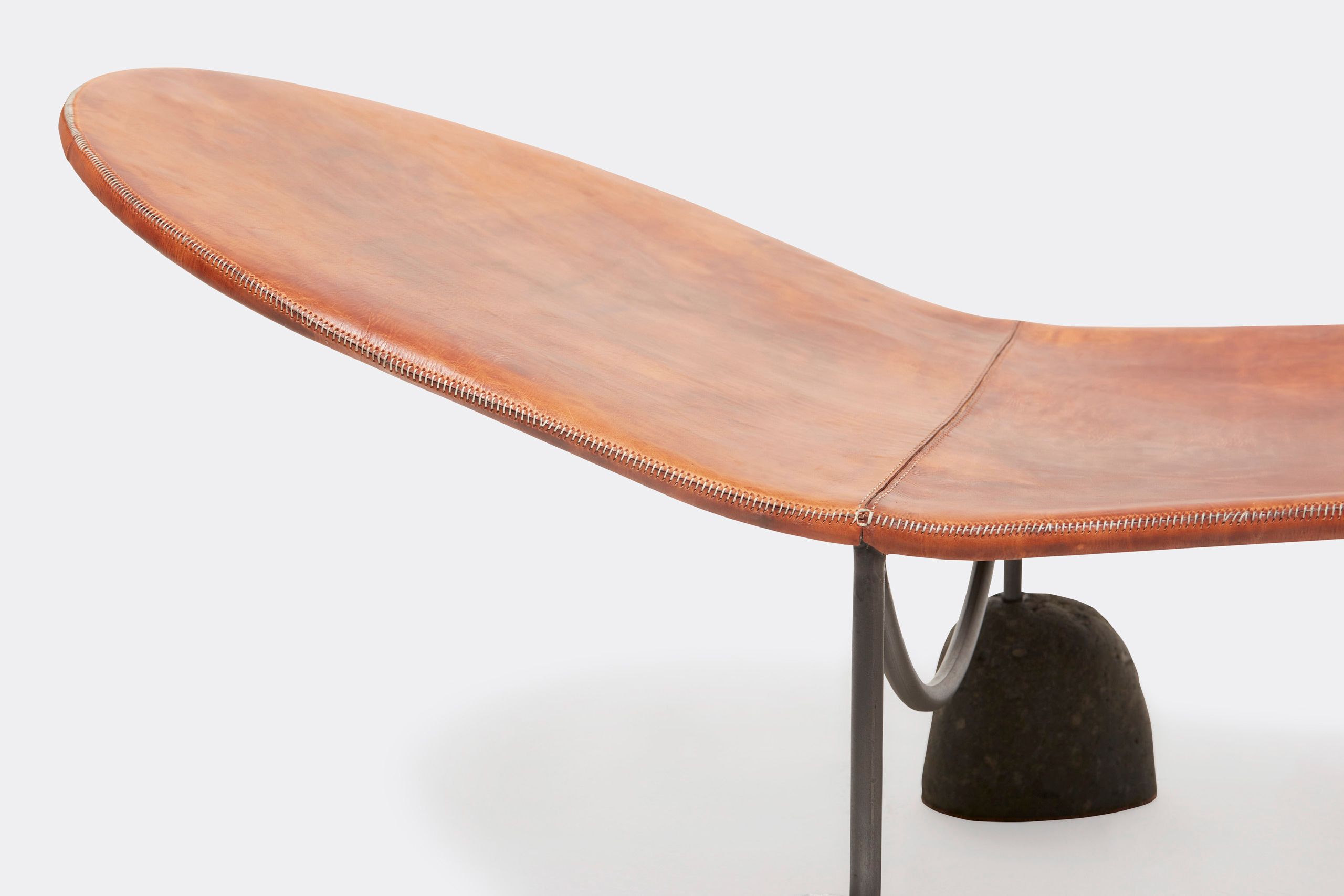 a brown leather chaise lounge with a steel frame and stone base shown on a white background .