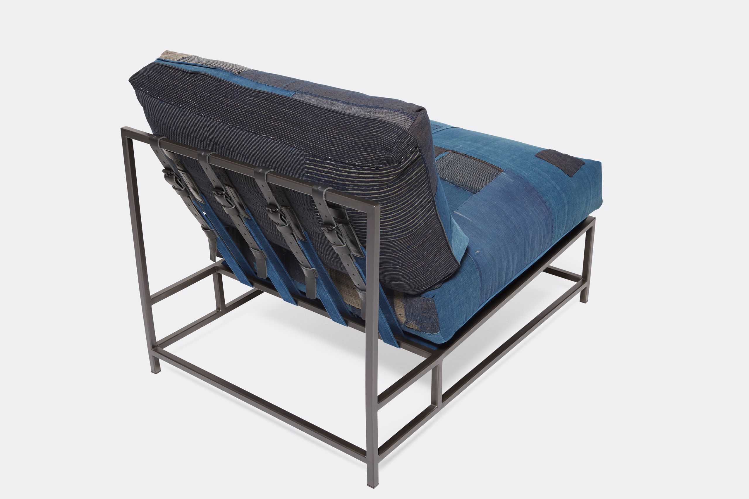 A steel framed chair upholstered with vintage japanese indigo and grey quilted material and blue and black supporting belts shown on a white background