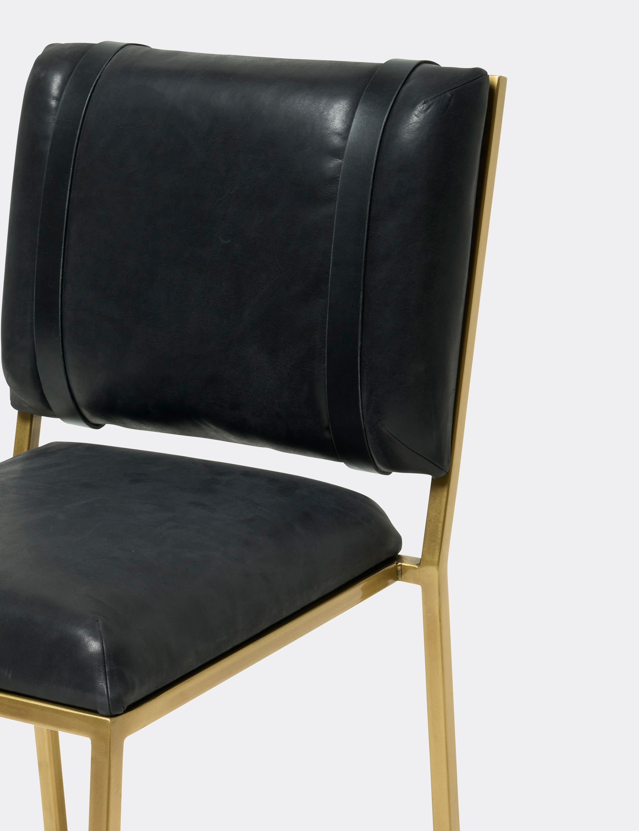 a black leather barstool with a brass finished steel frame and black leather belts shown on a white background .
