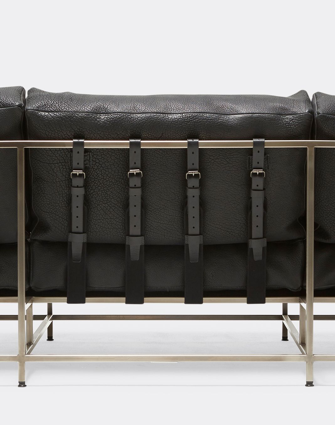 a black leather upholstered sofa with a nickel finished steel frame and black supporting belts shown on a white background .