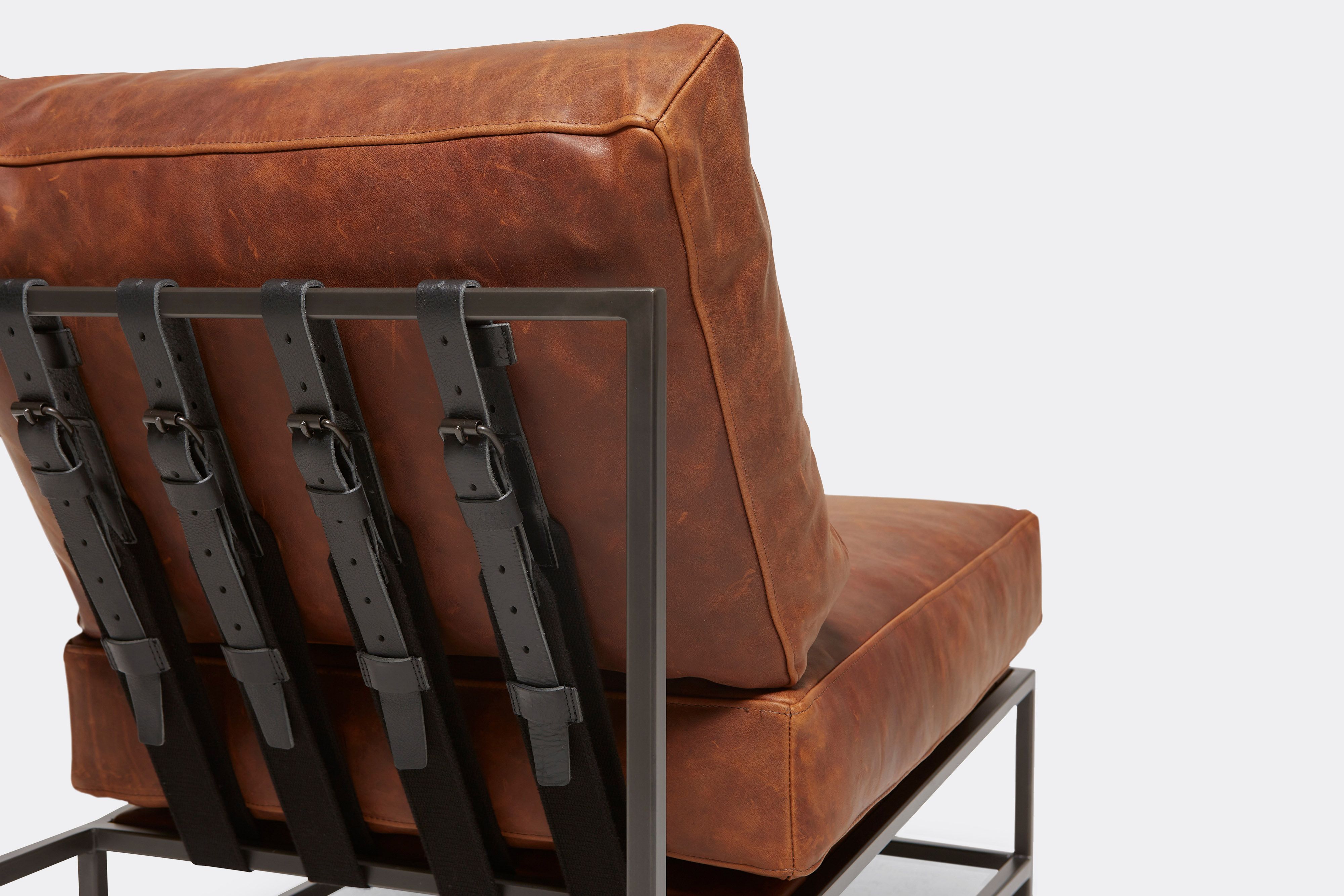 Back of lounge chair with brown leather upholstery and black leather belts on black metal frame