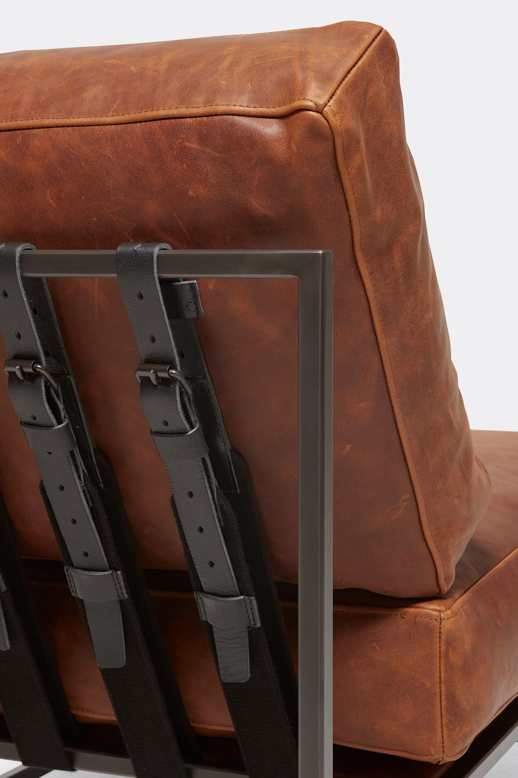 A brown leather chair with black leather and webbing belts and a blackened steel frame shown on a white background