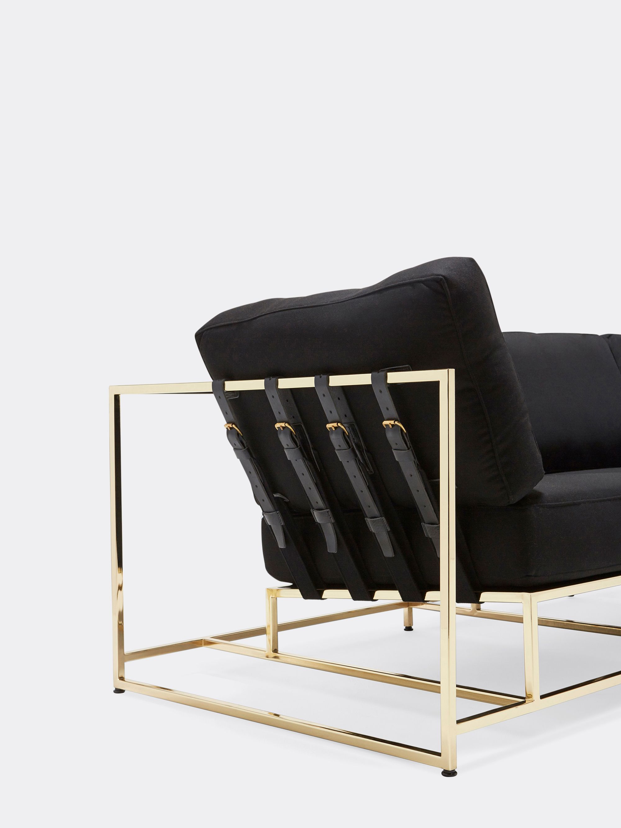 a black wool upholstered sofa with a polished brass finished steel frame on a and black supporting belts shown on a white background