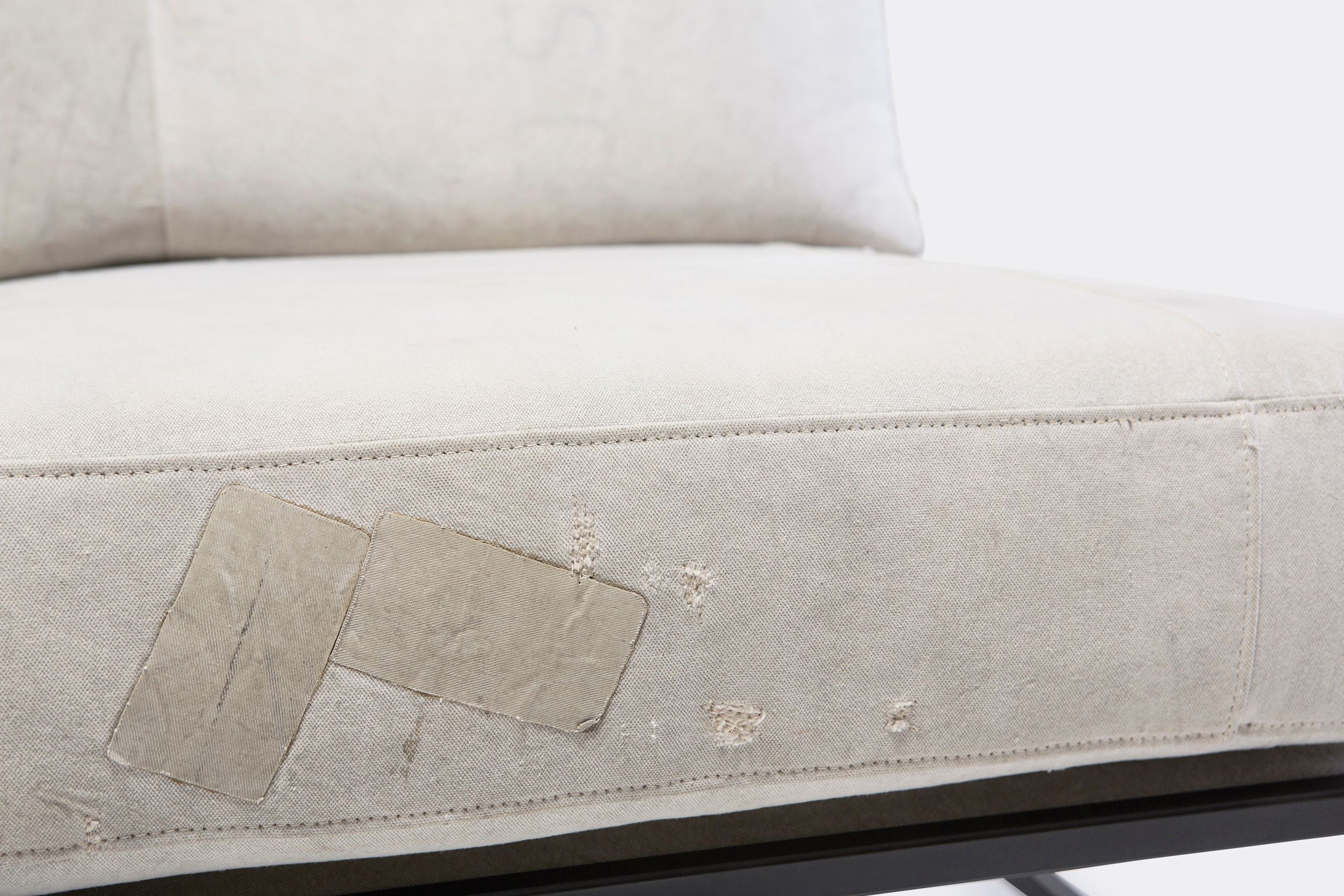A chair with a white cushion and leather straps atop a blackened steel frame on a white background