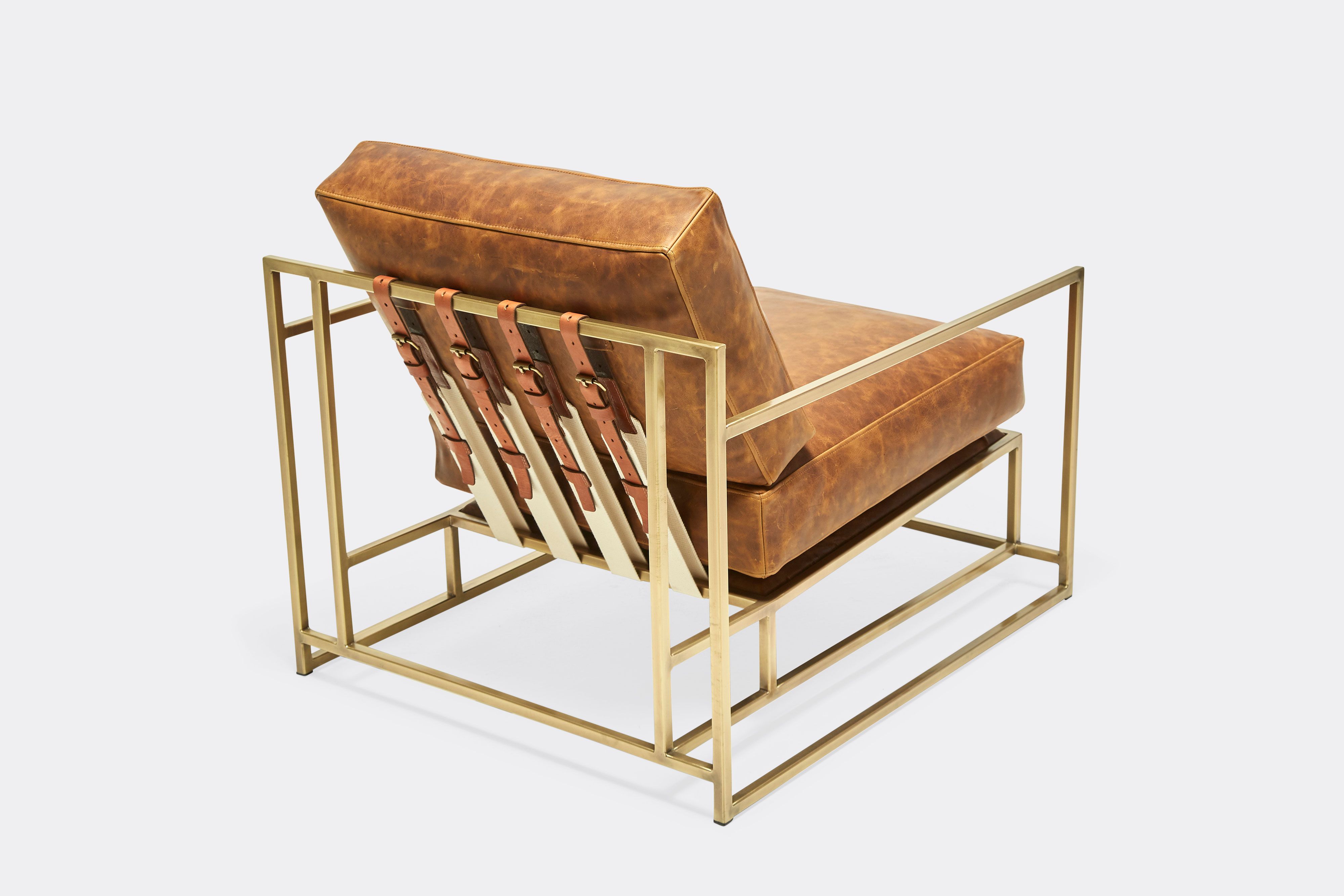 overhead of armchair with brown leather upholstery and brown leather belts on antique brass metal frame