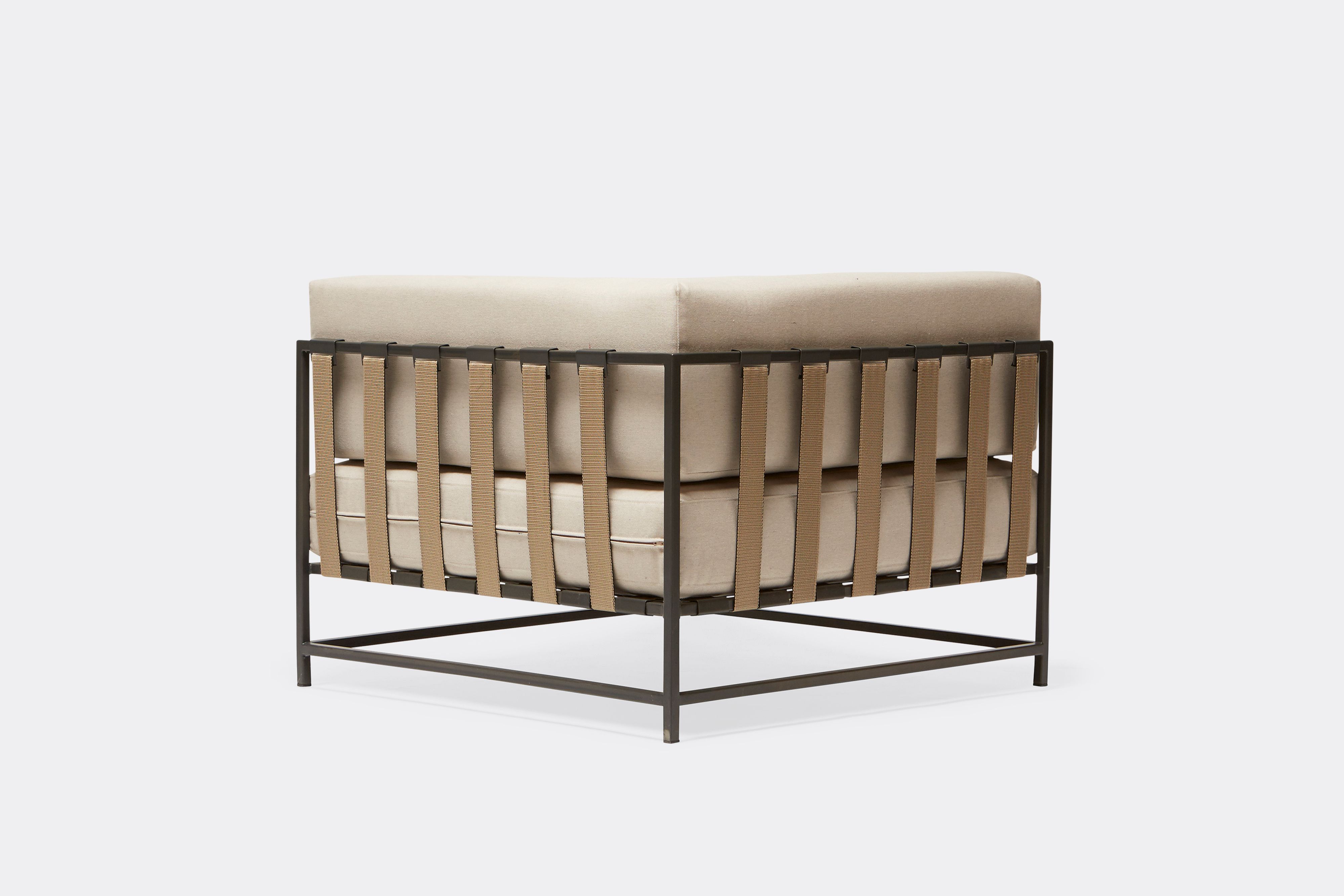 side of outdoor corner chair with cream canvas upholstery and tan belts on dark grey metal frame