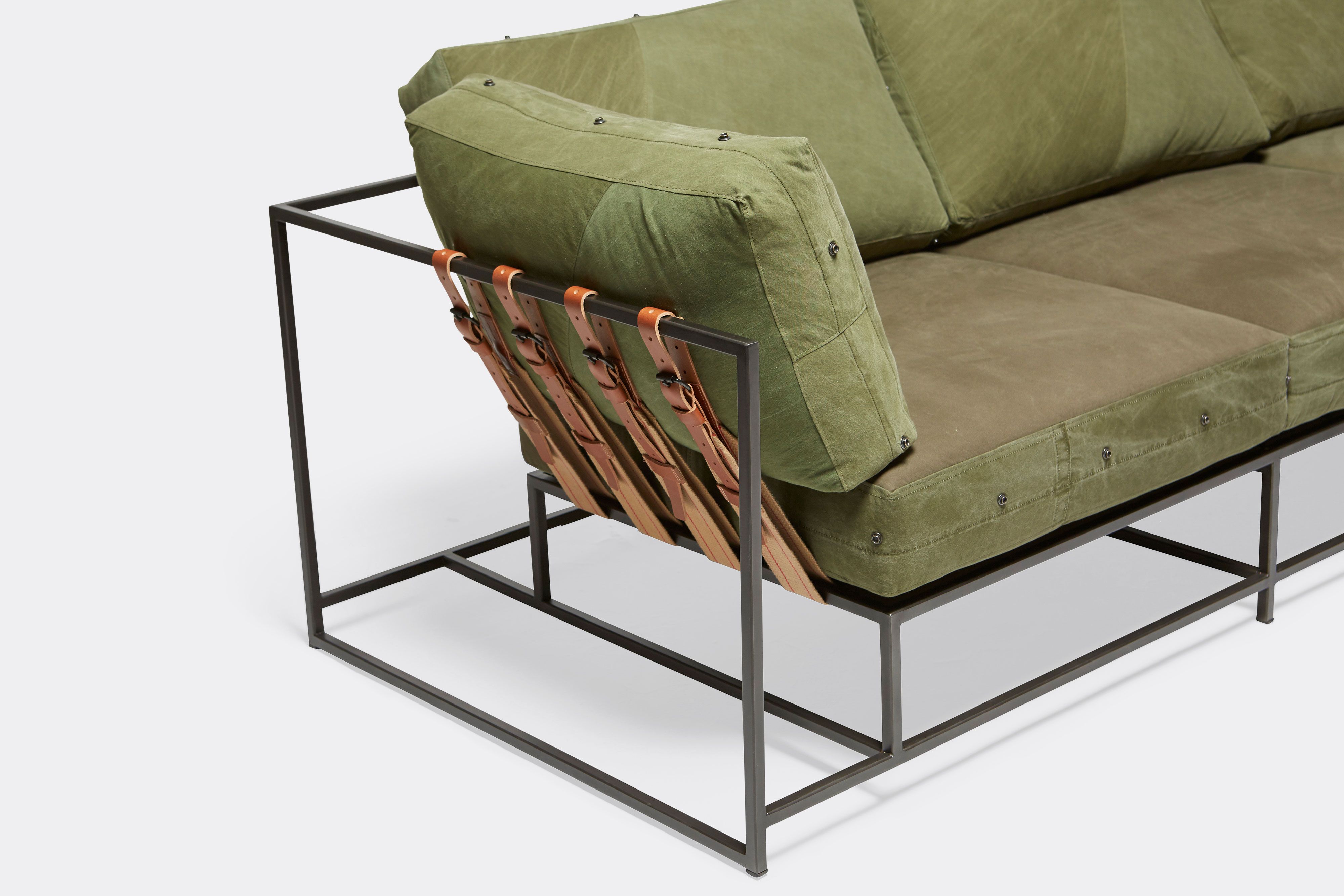 overhead detail of sectional with green canvas upholstery and brown leather belts on black metal frame