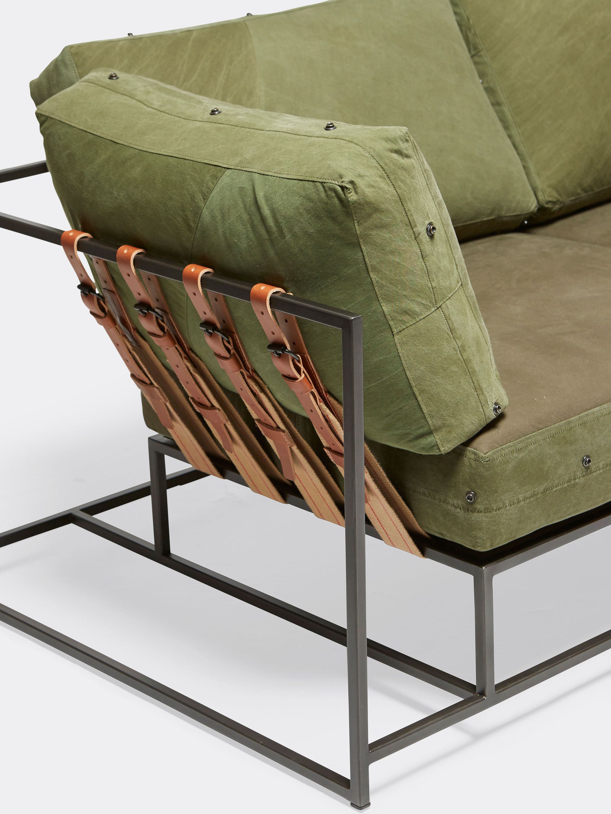 a sofa with green cushions and a metal frame and tan leather and webbing belts on a white background .