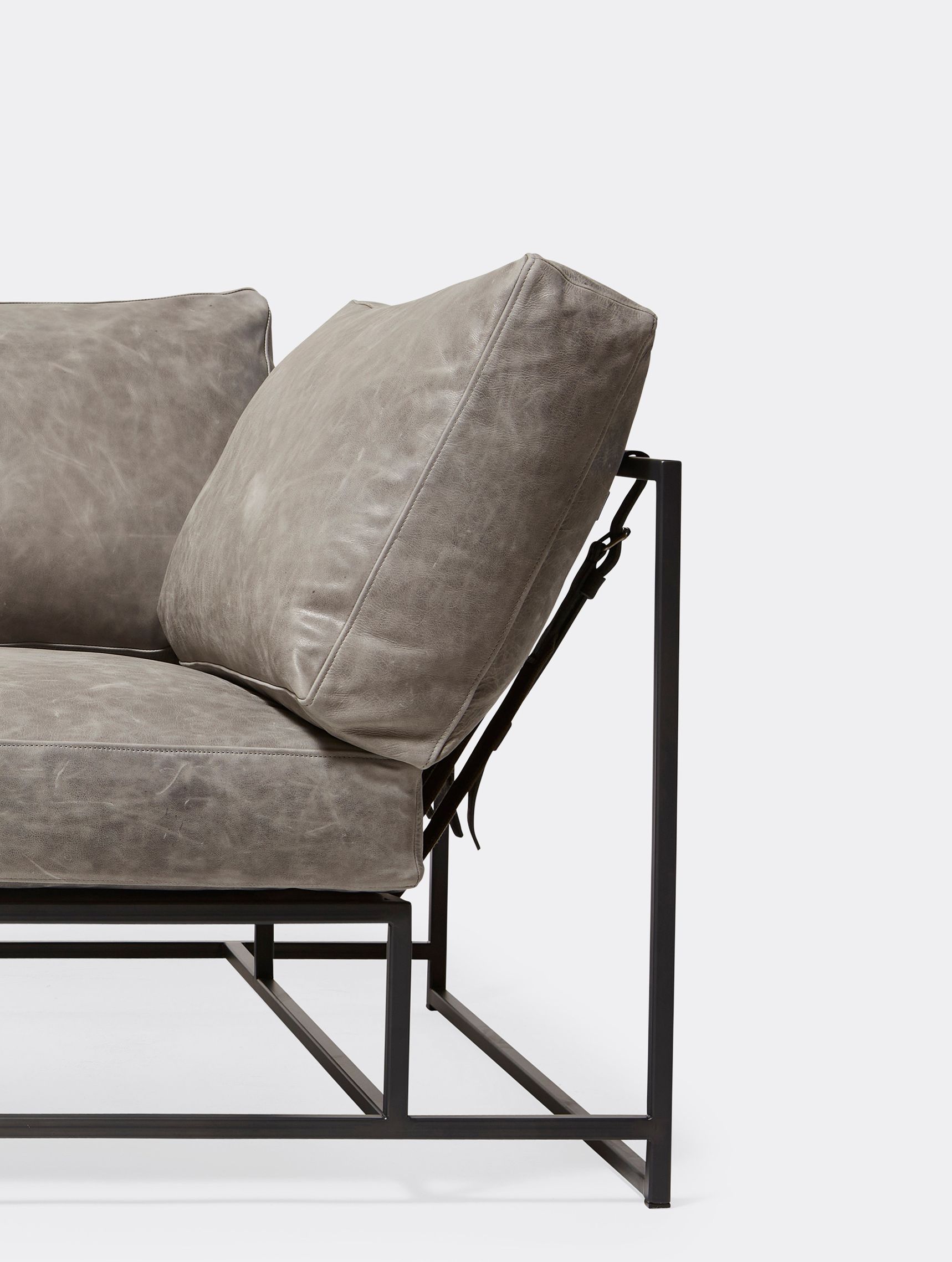 a grey leather upholstered sofa on a blackened steel frame with supporting belts shown on a white background