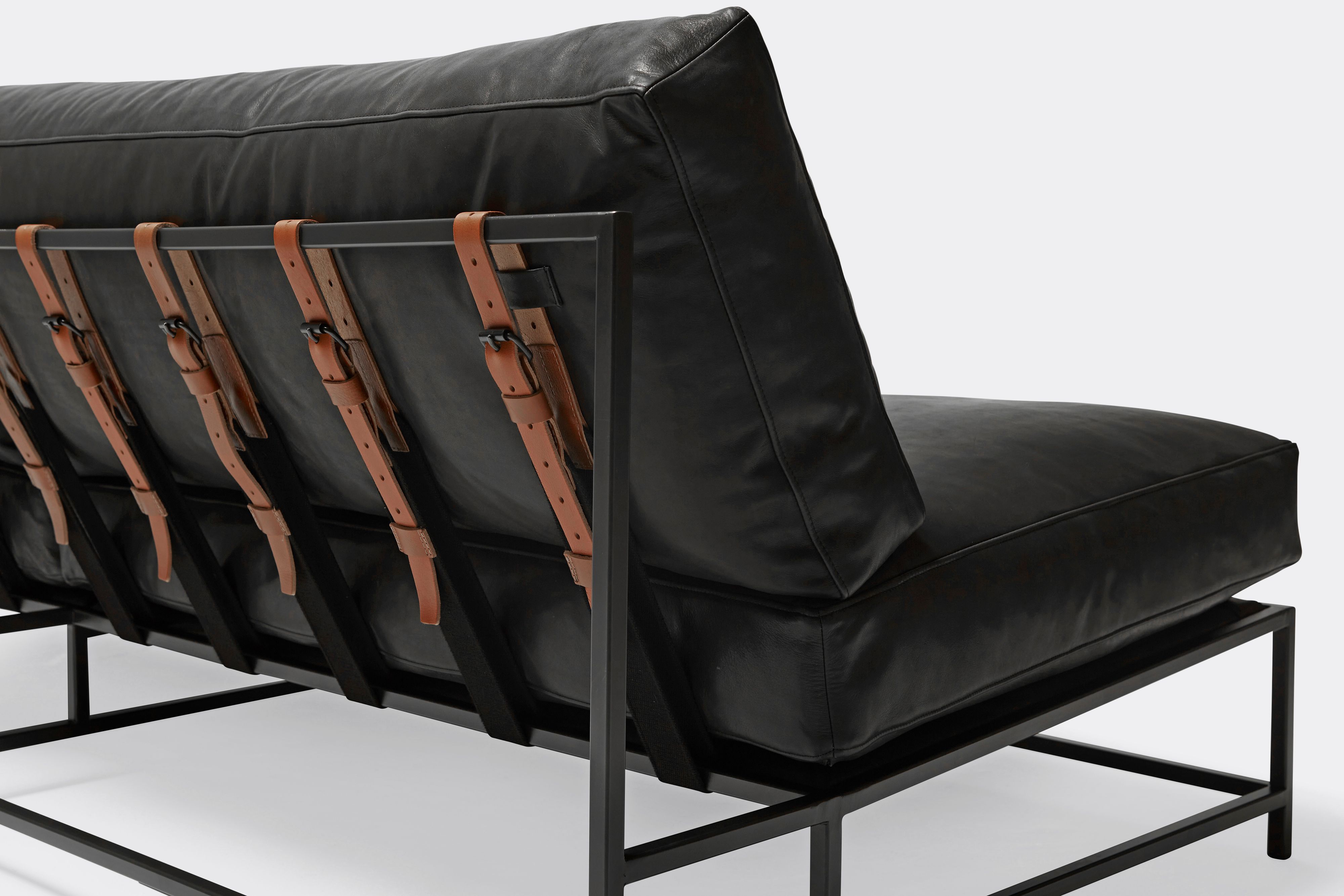detail of loveseat with black leather upholstery and brown leather belts on black metal frame