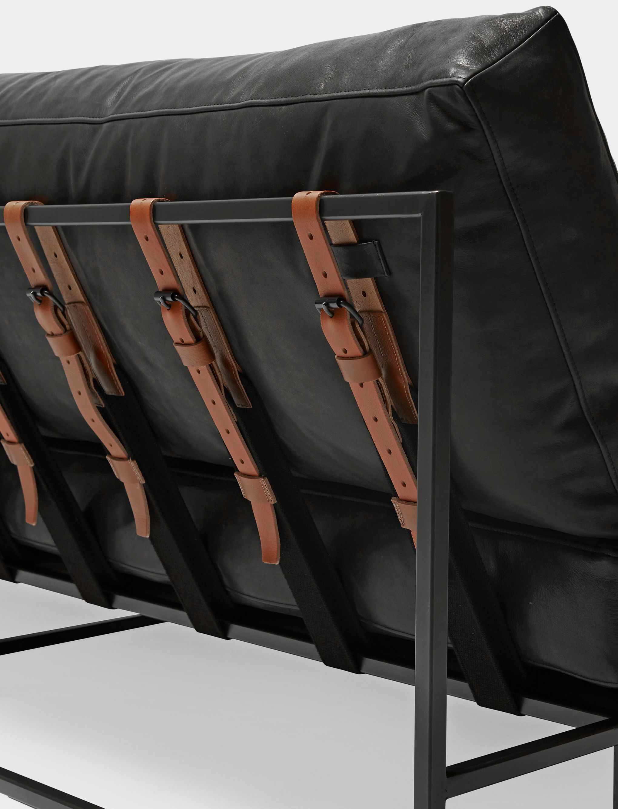  a black leather sofa with brown leather and webbing belts on a blackened steel frame shown on a white background