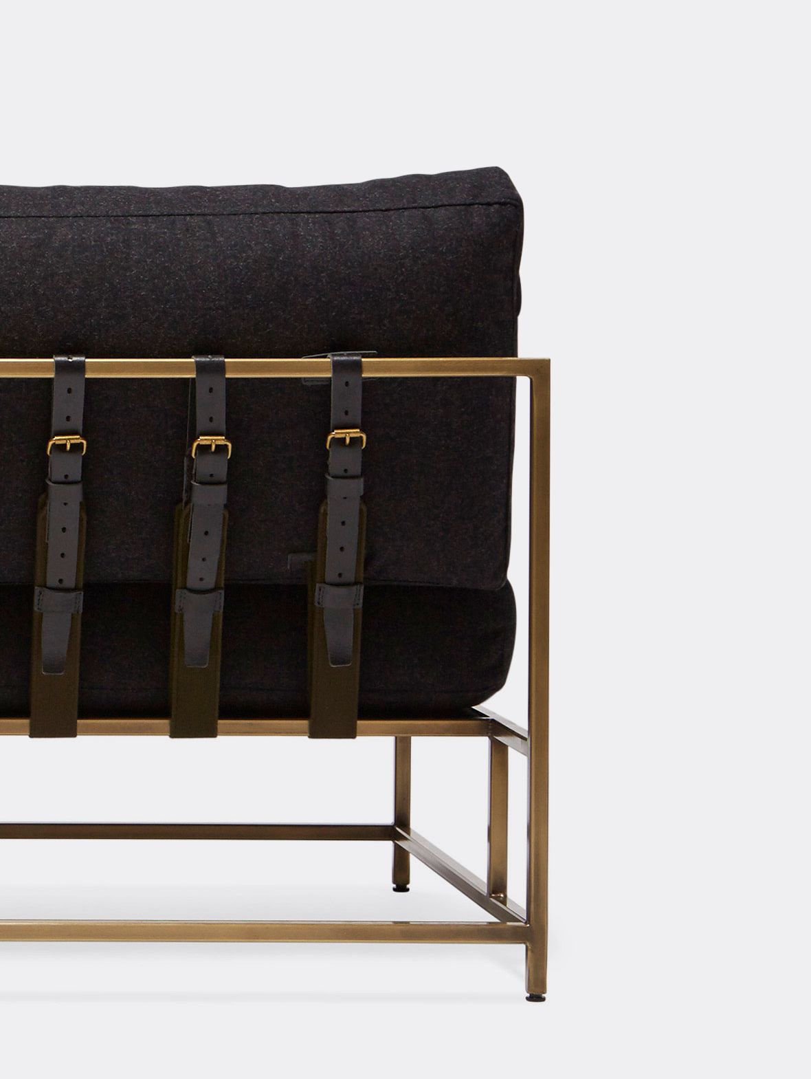 a black wool upholstered loveseat with antique brass frame finish and black supporting belts shown on a white background .